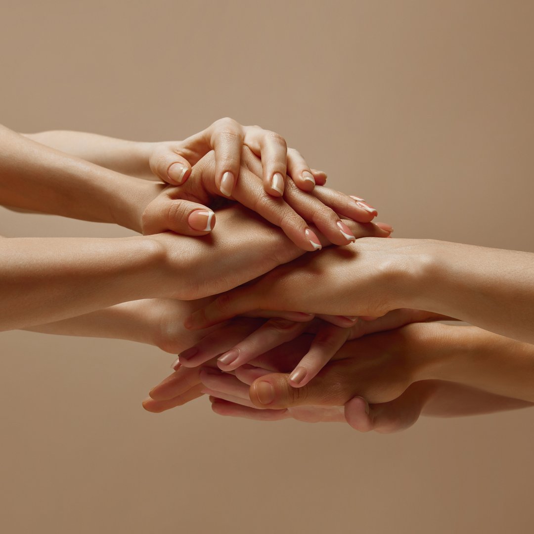 Various woman puts his hands together showcasing unity, teamwork and support against beige studio background. Concept of human touch, beauty and care, spa procedures.