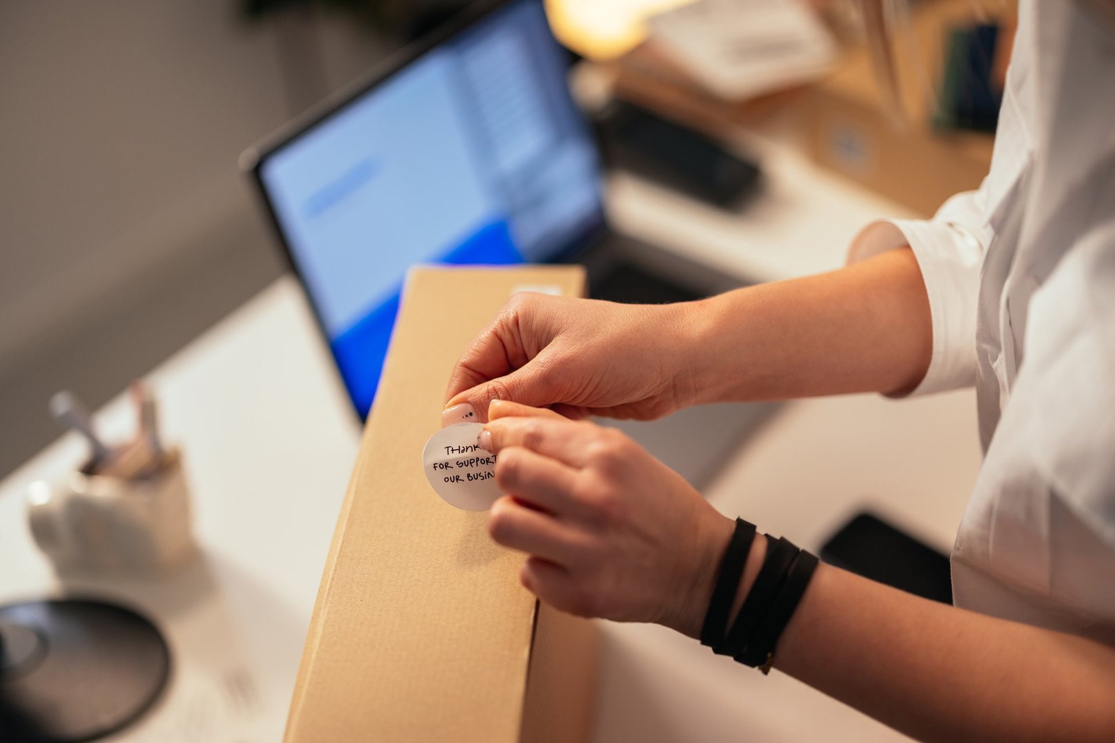 Hands of a businessperson carefully placing a 'Thank you' note on a cardboard box, emphasizing customer appreciation