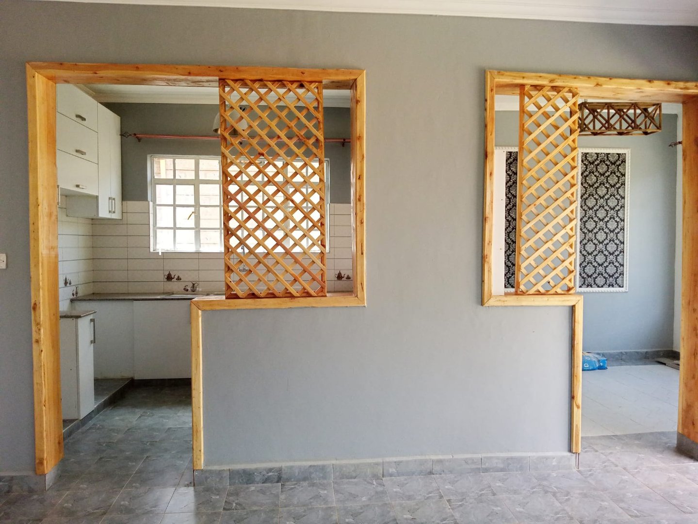 Interior view of a modern kitchen with open wooden lattice partitions and a grey tiled floor.