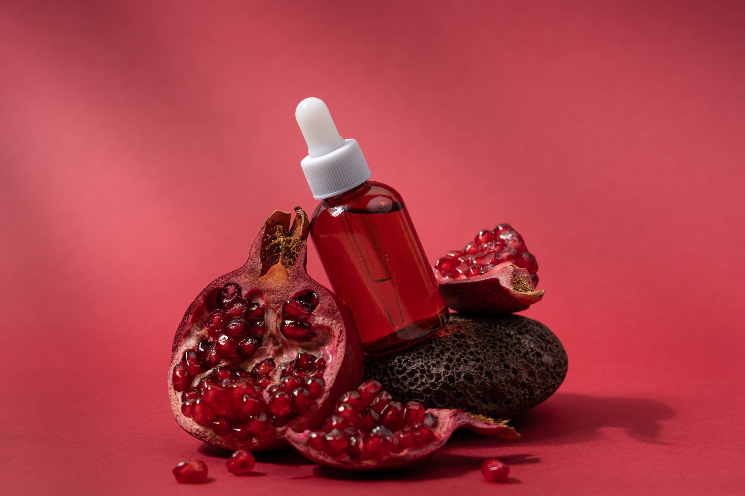 Cosmetic serum in bottle with slice of juicy ripe pomegranate on red background with copy space