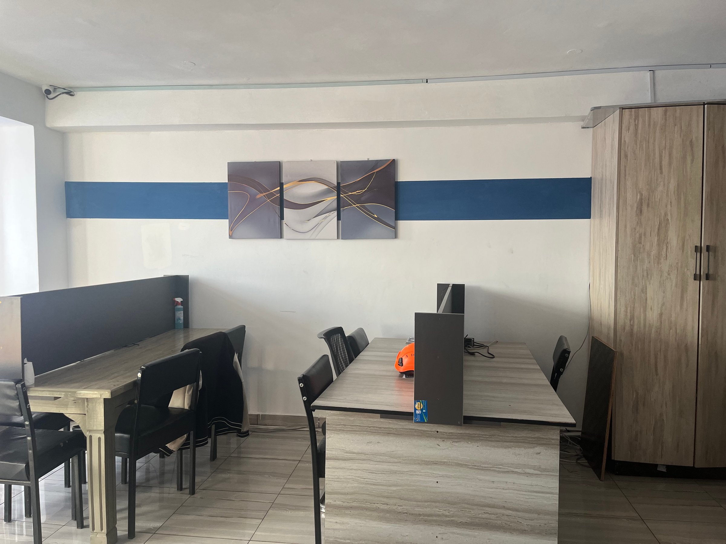 Office space with desks, chairs, a wall painting, and a wooden cabinet in a minimalist design.