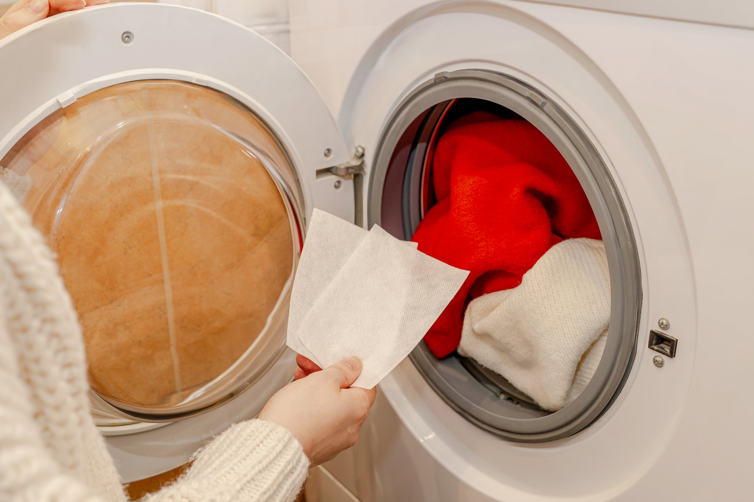 Color catcher sheet used during laundry.  Hand holding a color catcher sheet before placing it in the washing machine with red and white clothes to prevent dye transfer.