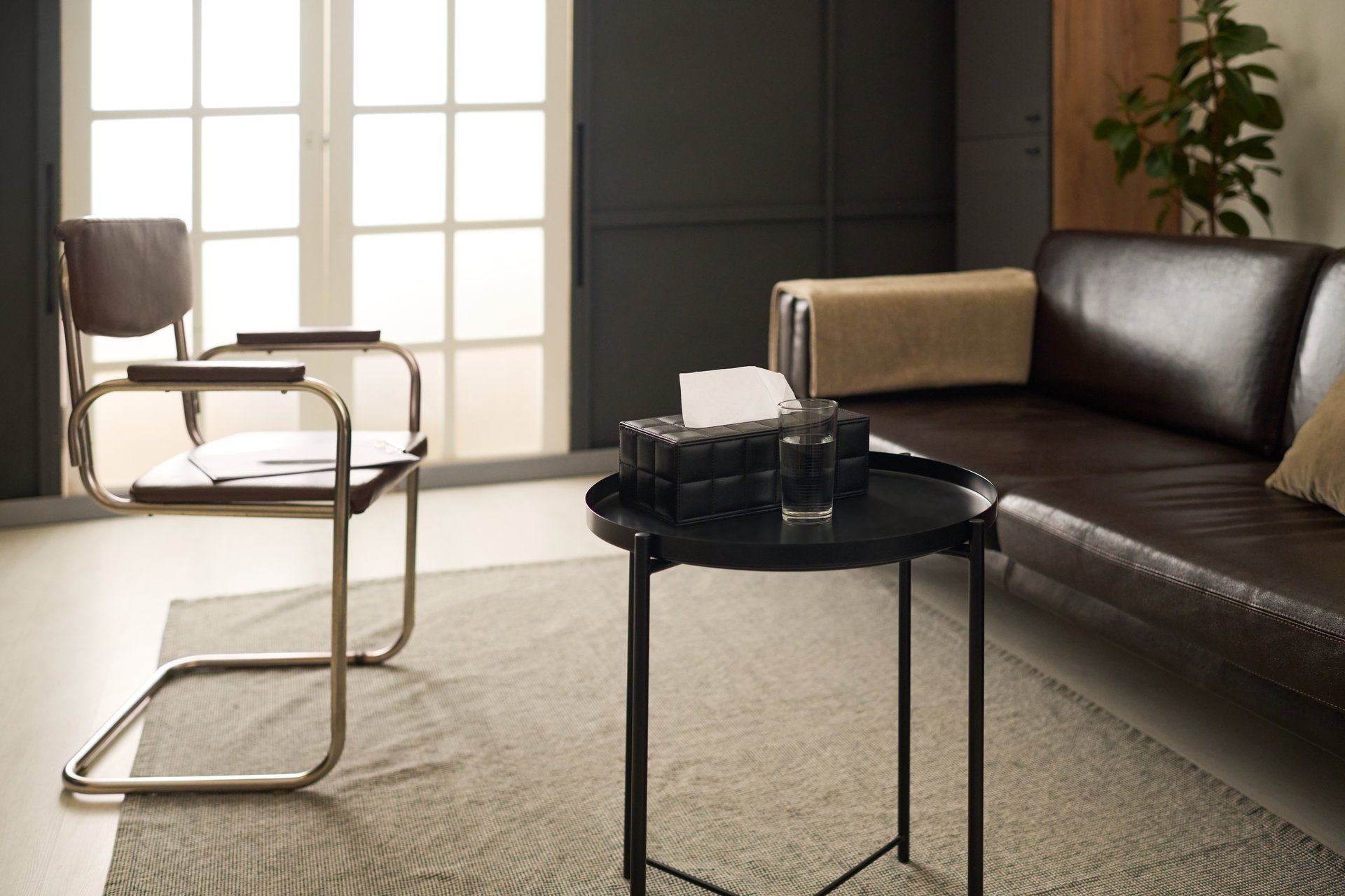 Background image of sleek therapy room interior with comfortable couch and calming earthy tones with low lighting and tissue box on table, copy space
