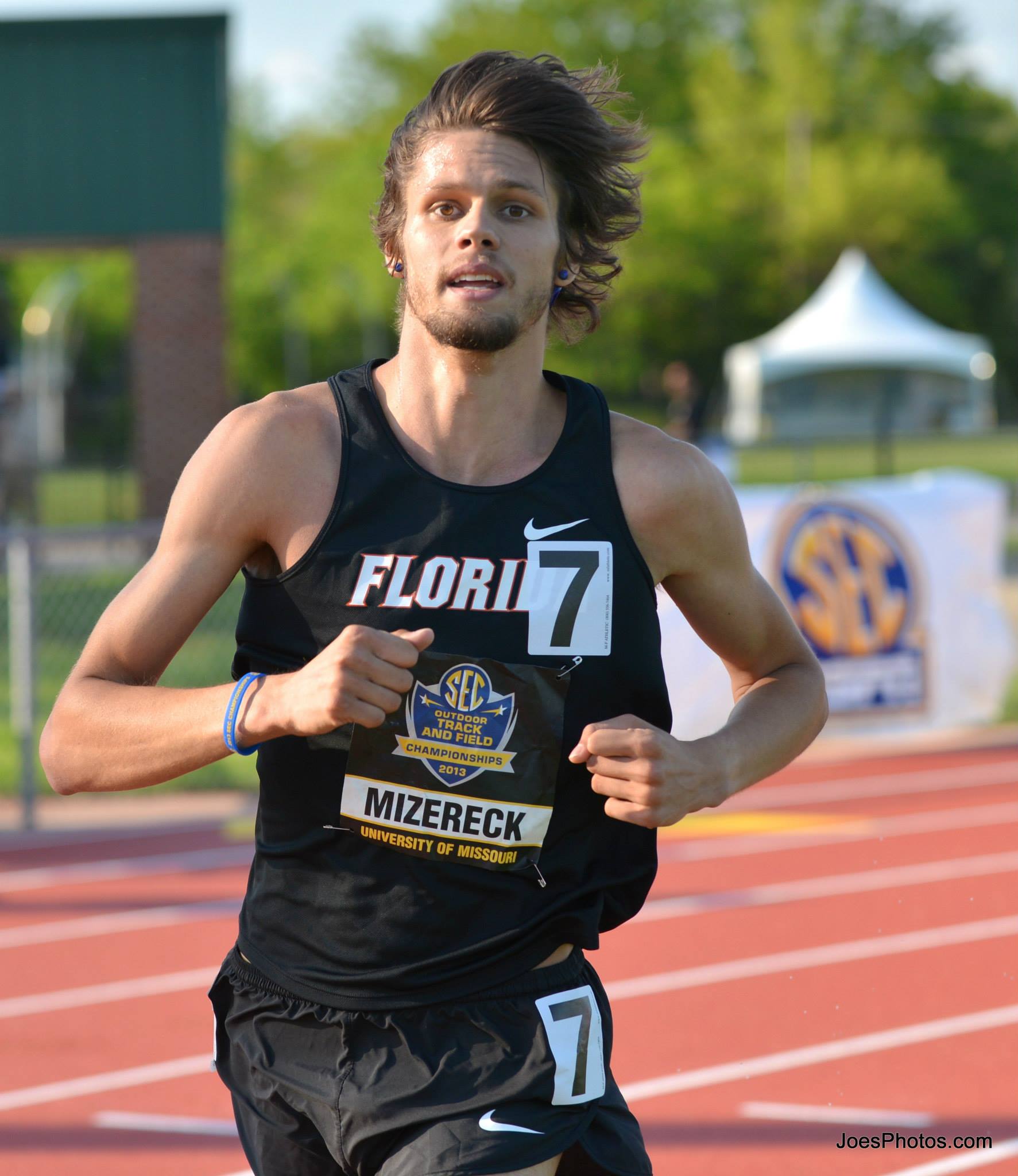Male athlete running on a track wearing a black athletic outfit with number 7 during a track and field event.