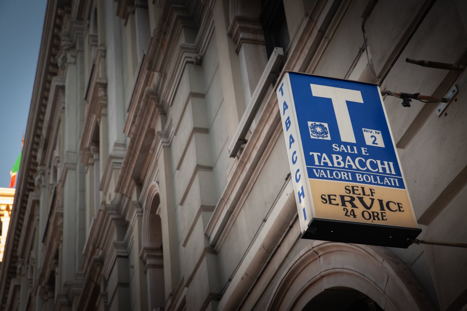Trieste, Italie - 19 décembre 2024 : Cette photographie capture le panneau reconnaissable du magasin Tabacchi bleu et blanc, une marque de fabrique des bureaux italiens, affiché sur une façade en pierre ornée. Dans ces établissements agréés par le gouvernement, les clients peuvent acheter des produits du tabac, des timbres fiscaux et des billets de loterie. L'image souligne l'importance culturelle et économique durable des magasins de tabac à travers l'Italie, faisant écho à la fois à la tradition et à la commodité moderne.