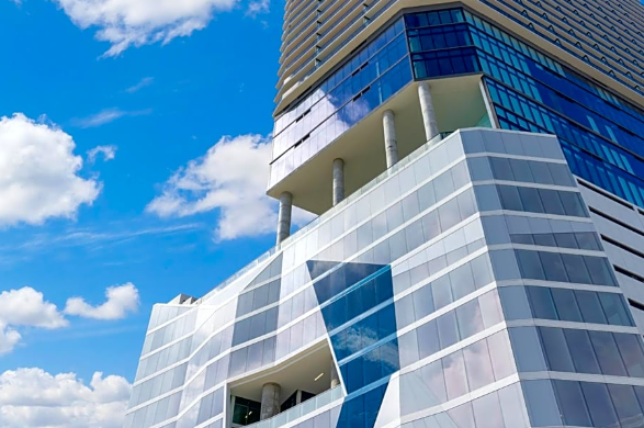 Modern building with geometric glass facade and columns against a blue sky with clouds.