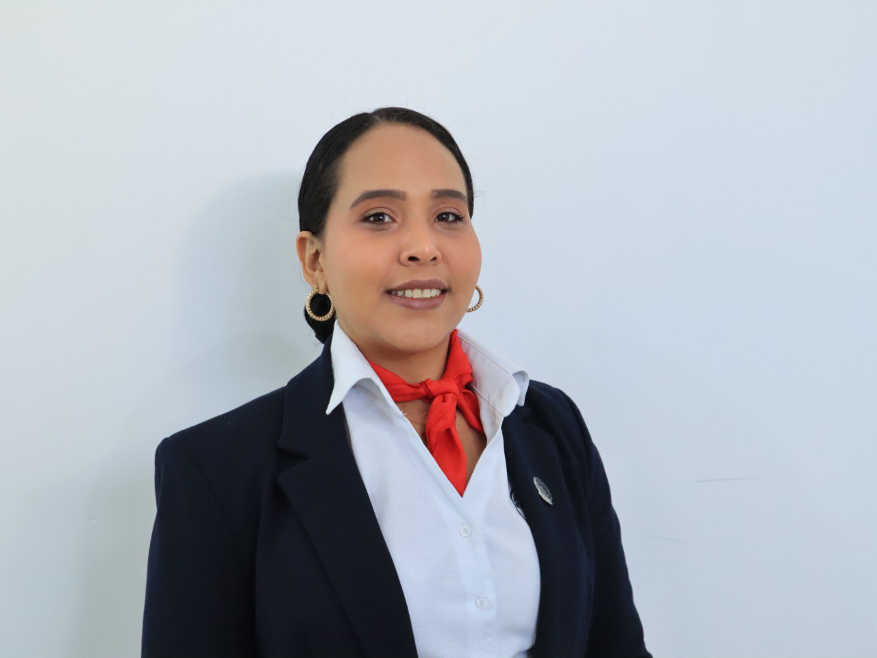 Woman in a formal uniform with a red neckerchief and hoop earrings, smiling against a plain background.
