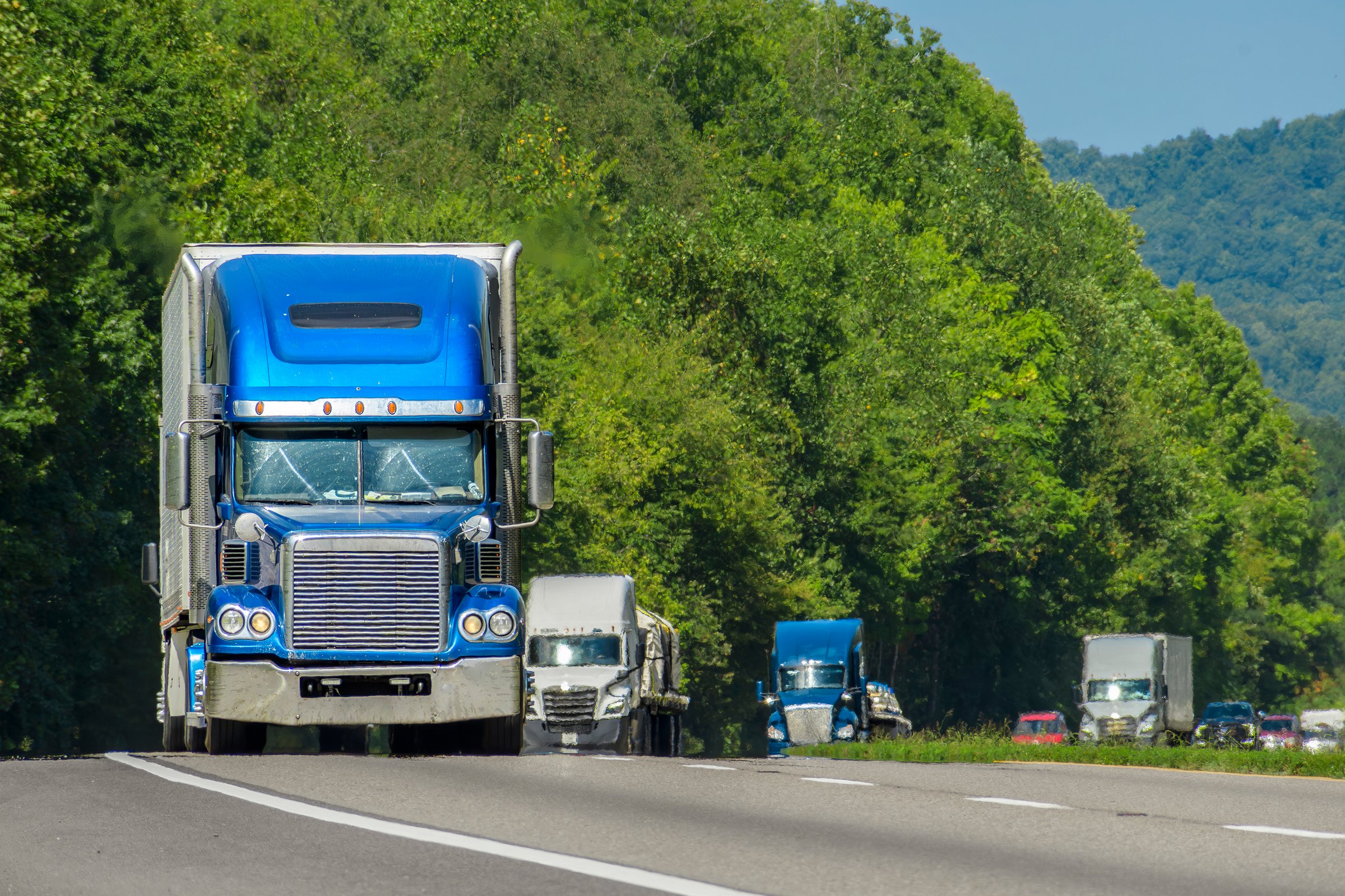 A blue semi leads a line of traffic down an Interstate in eastern Tennessee. Heat waves rising from the hot asphault creates a blurring effect on background trucks and foreground pavement.