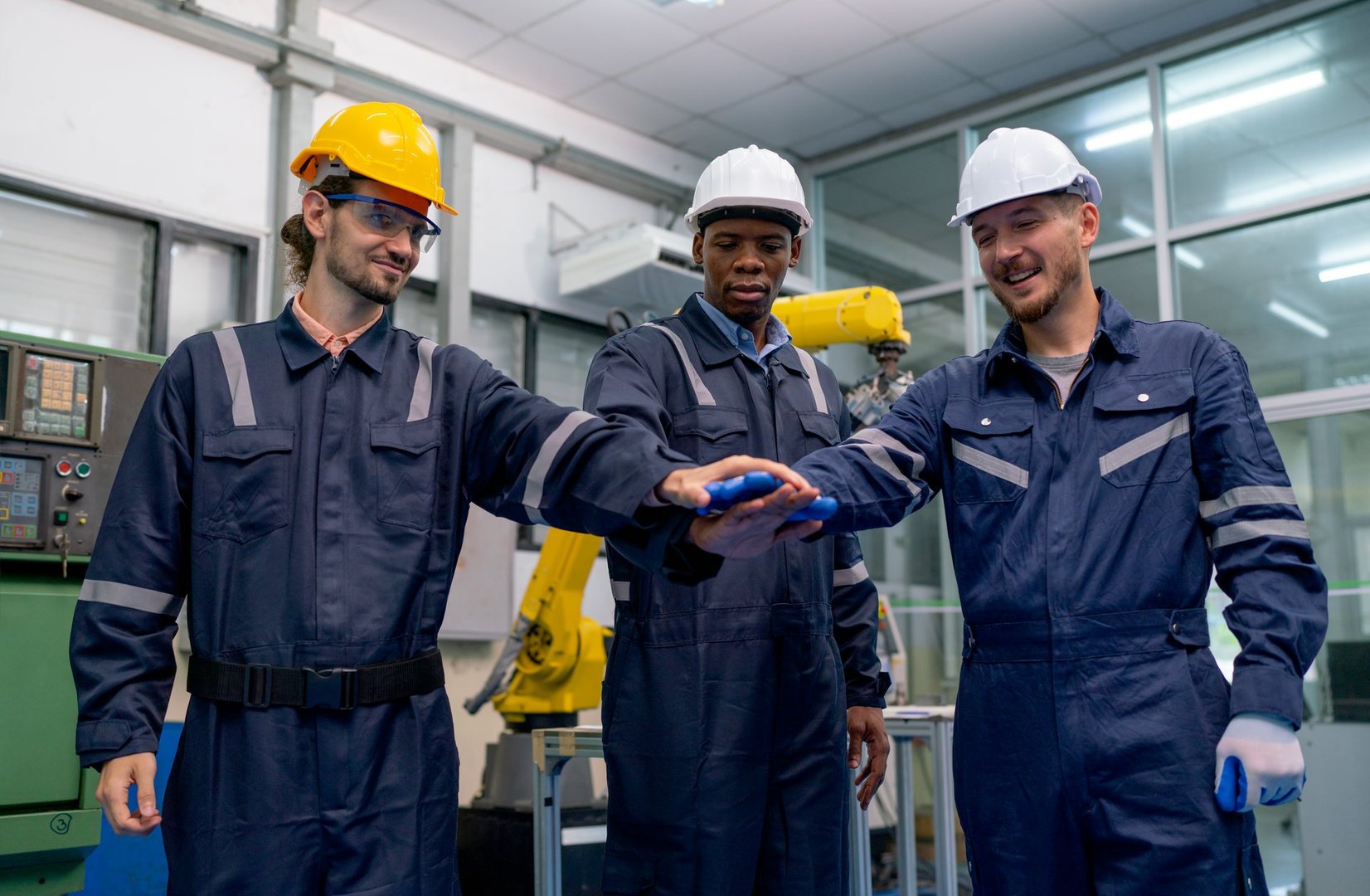 African American technician or engineer man hold hands together with Caucasian co-workers and stand in front of robotic arm in factory workplace.