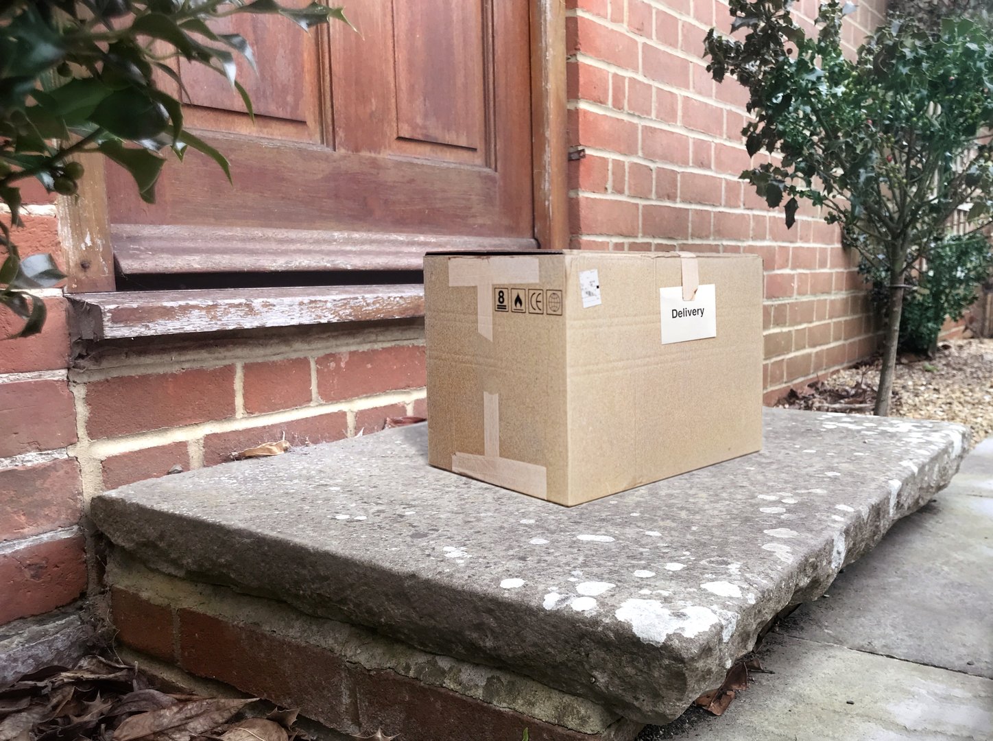 A generic package is on a doorstep, waiting for pickup by the homeowner. It has a label saying "delivery". Photographic composite.