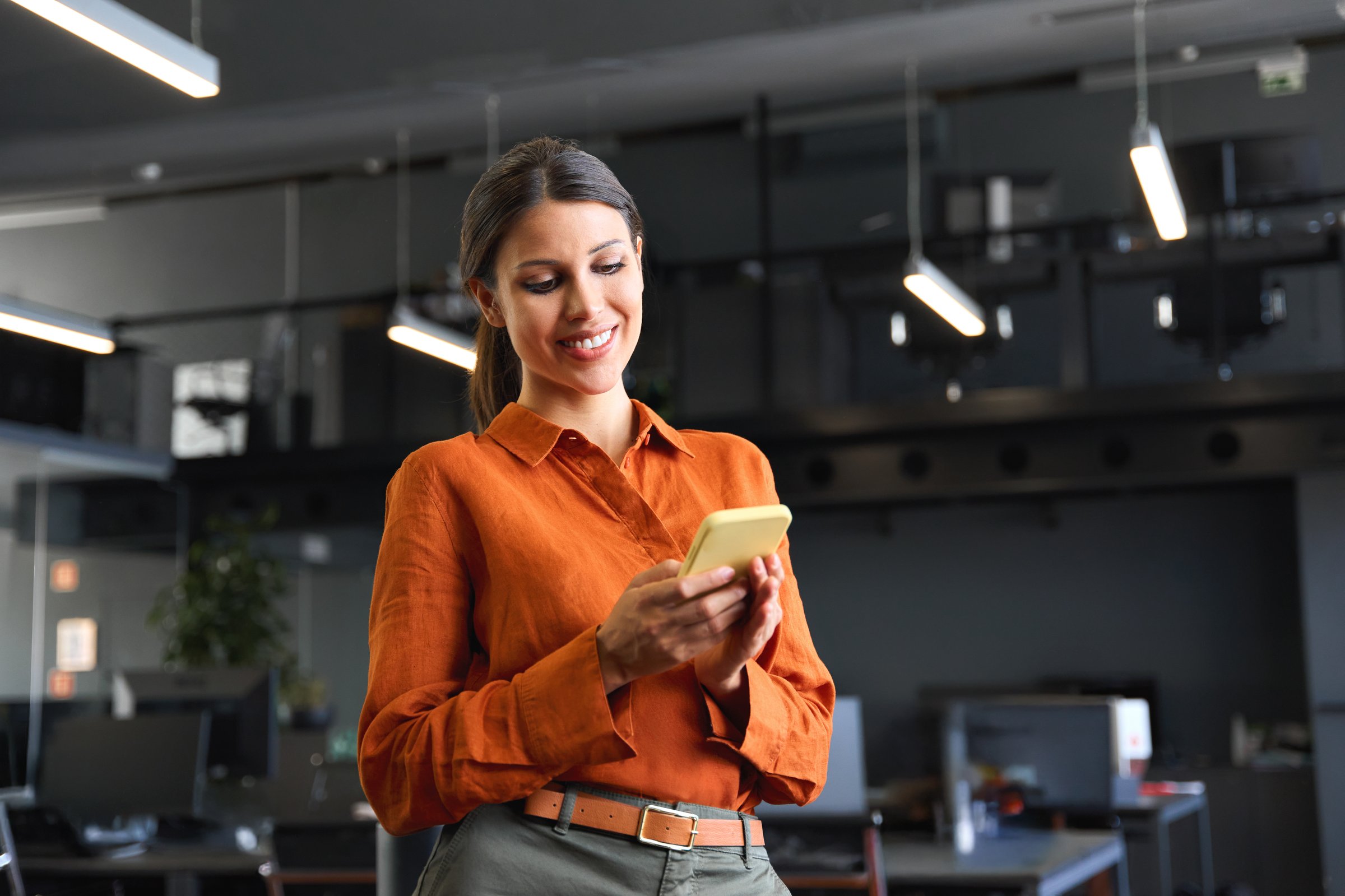 Young Indian business woman manager ceo using cell phone mobile application. Smiling Latin Hispanic mature female businesswoman holding smartphone in office trading app, working online. Copy space