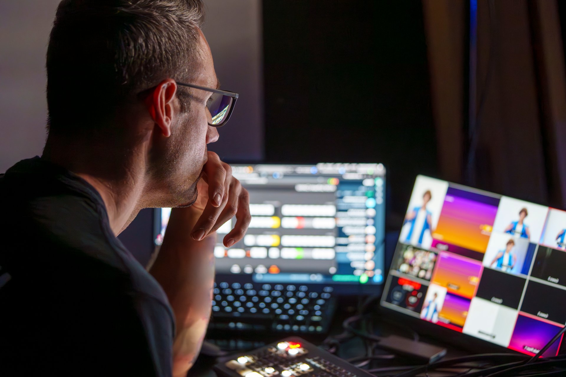 Male mature video director managing multiple screens and equipment in a control room during a live broadcast