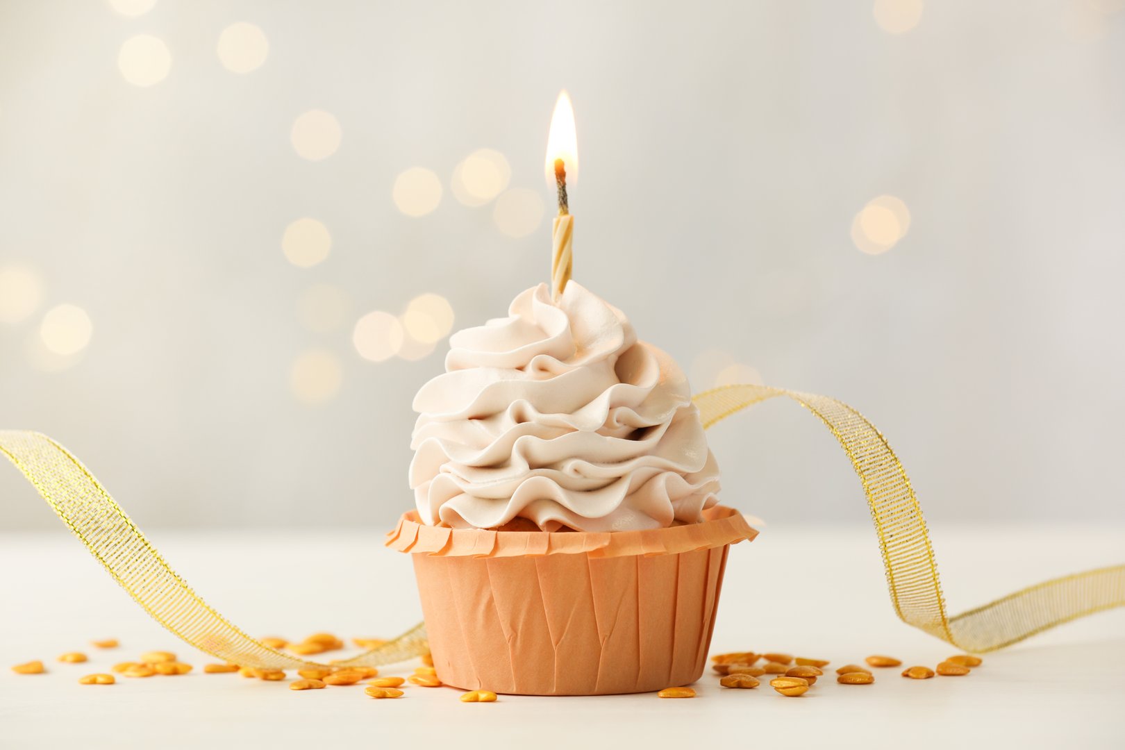 Birthday cupcake with burning candle on light table against blurred lights