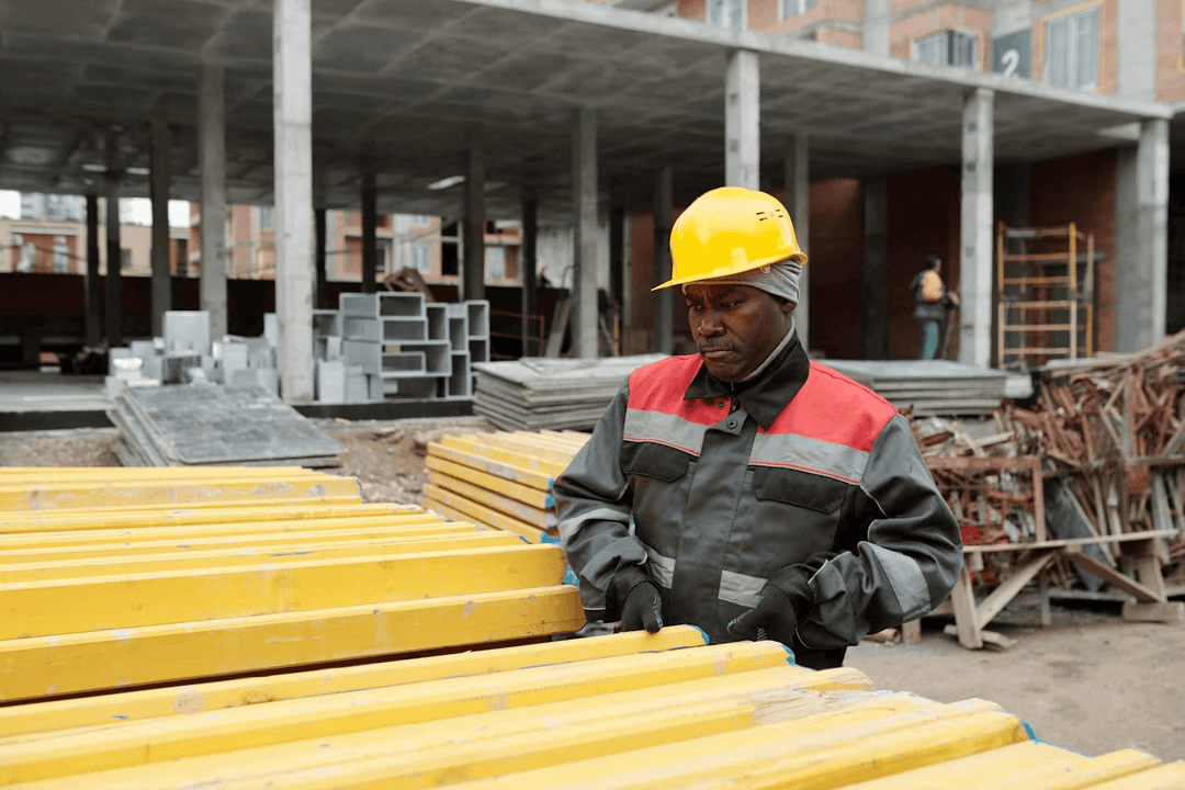 Construction worker in a yellow hard hat handling materials at a building site. Concrete structure visible in background.