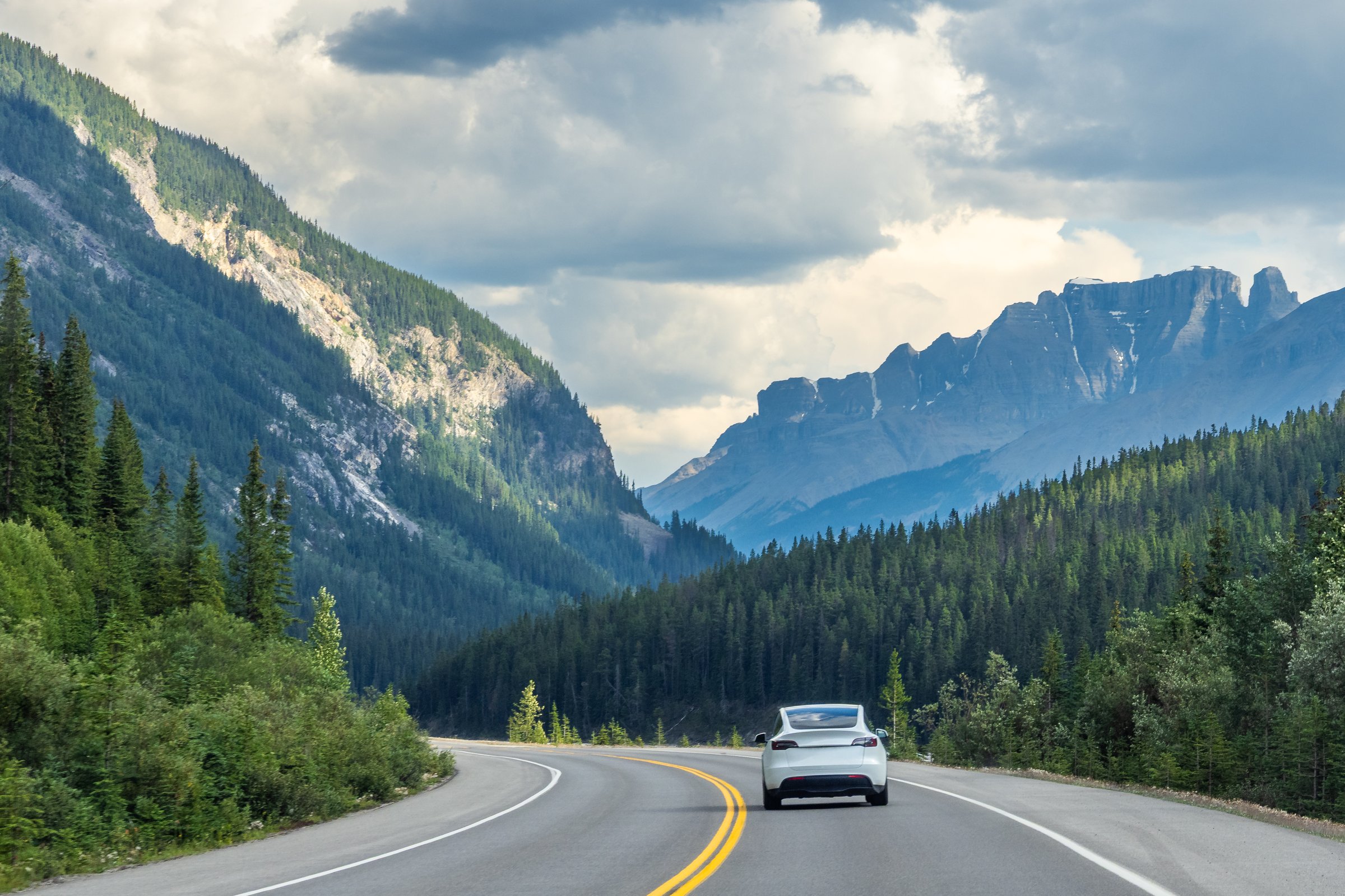 Car driving along Icefields Parkway toward towering Rocky Mountains