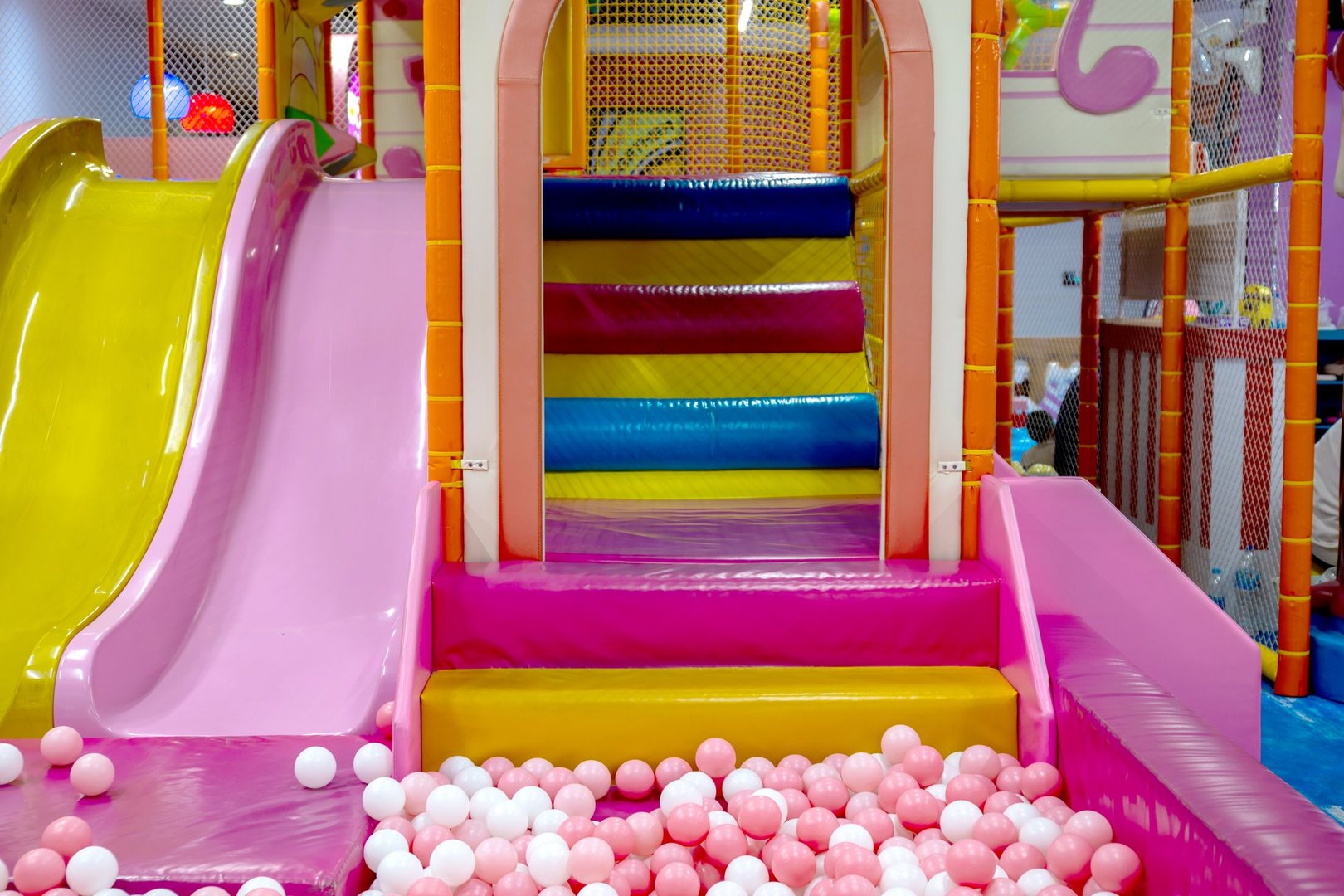 Colorful indoor playground with multicolored steps, pink and yellow slides, and a pink-white ball pit, creating a fun and safe play environment for children