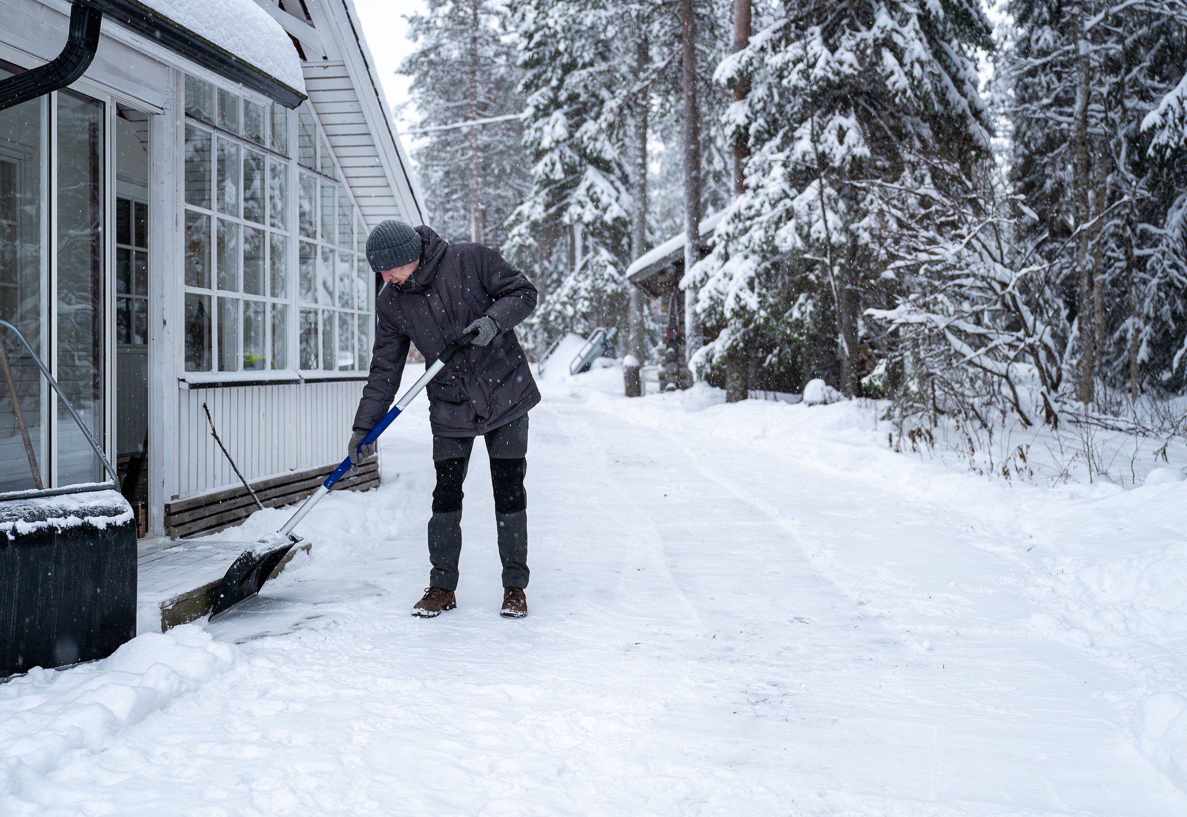 man clearing snow using a snow shovel with a snowy outdoor background. Winter task concept