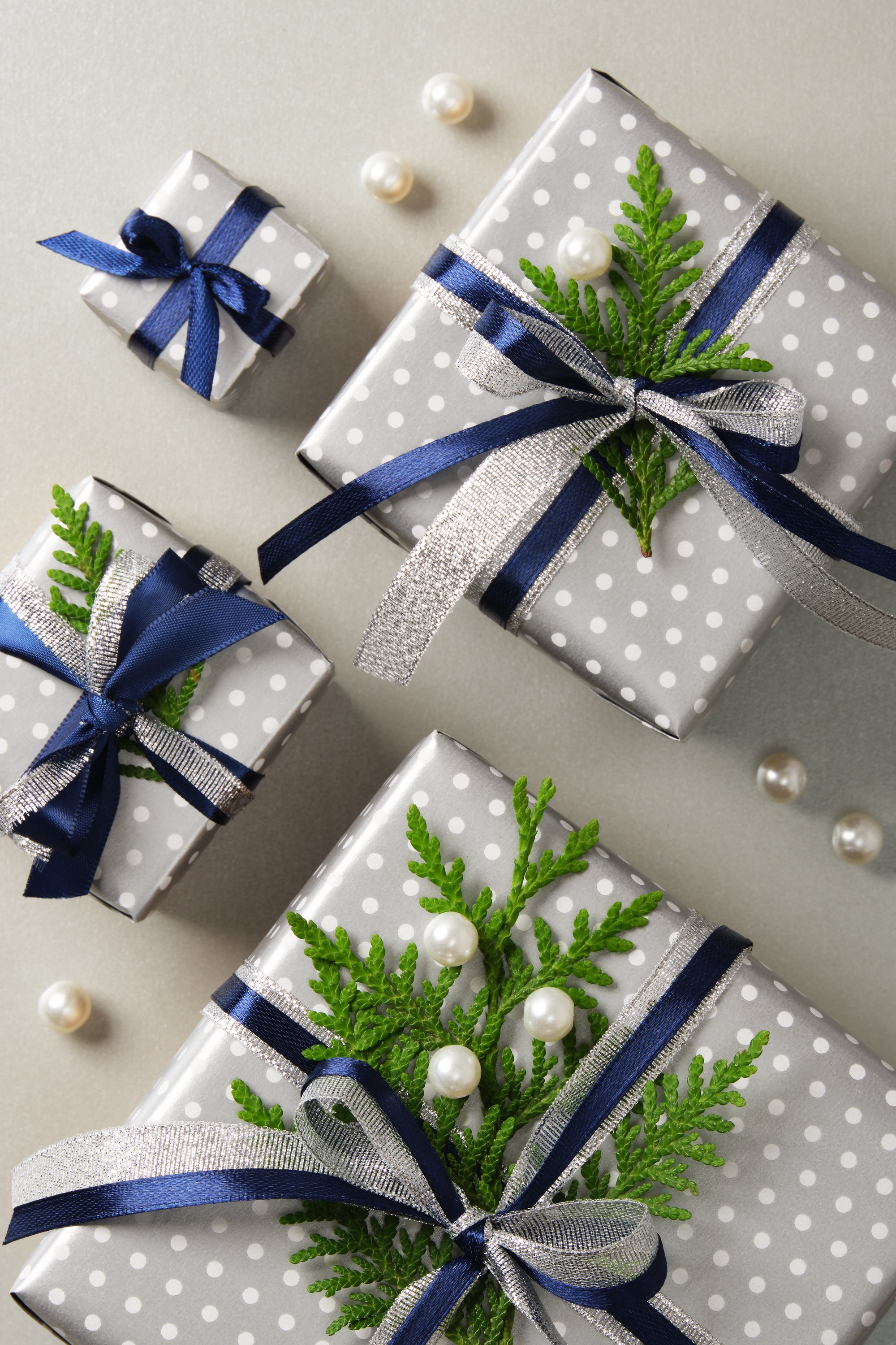 Neatly arranged silver gift boxes with blue ribbons and sprigs of thuja. Gray background