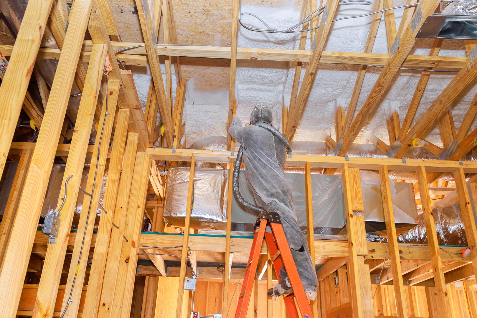 Worker applying spray foam to ceiling beams