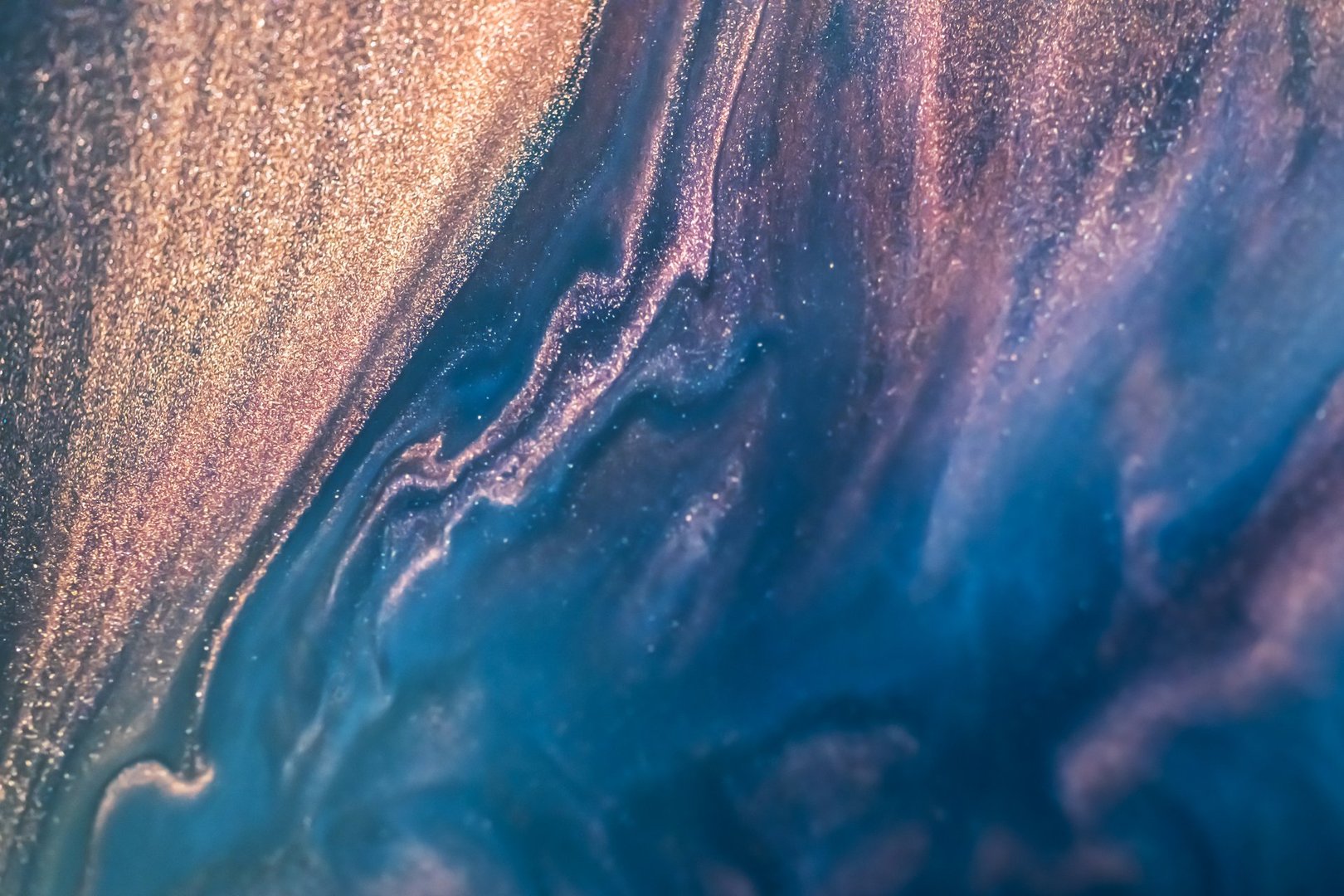 Colorful liquid paint abstract background. Blue and purple acrylic paints with golden glitter blending texture.