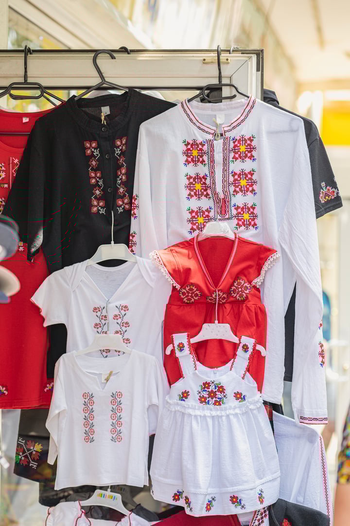 Embroidered traditional national bulgarian shirts and folk dresses for adults and children hanging at colorful market stall. Concept of family heritage, ethnic clothing, cultural identity