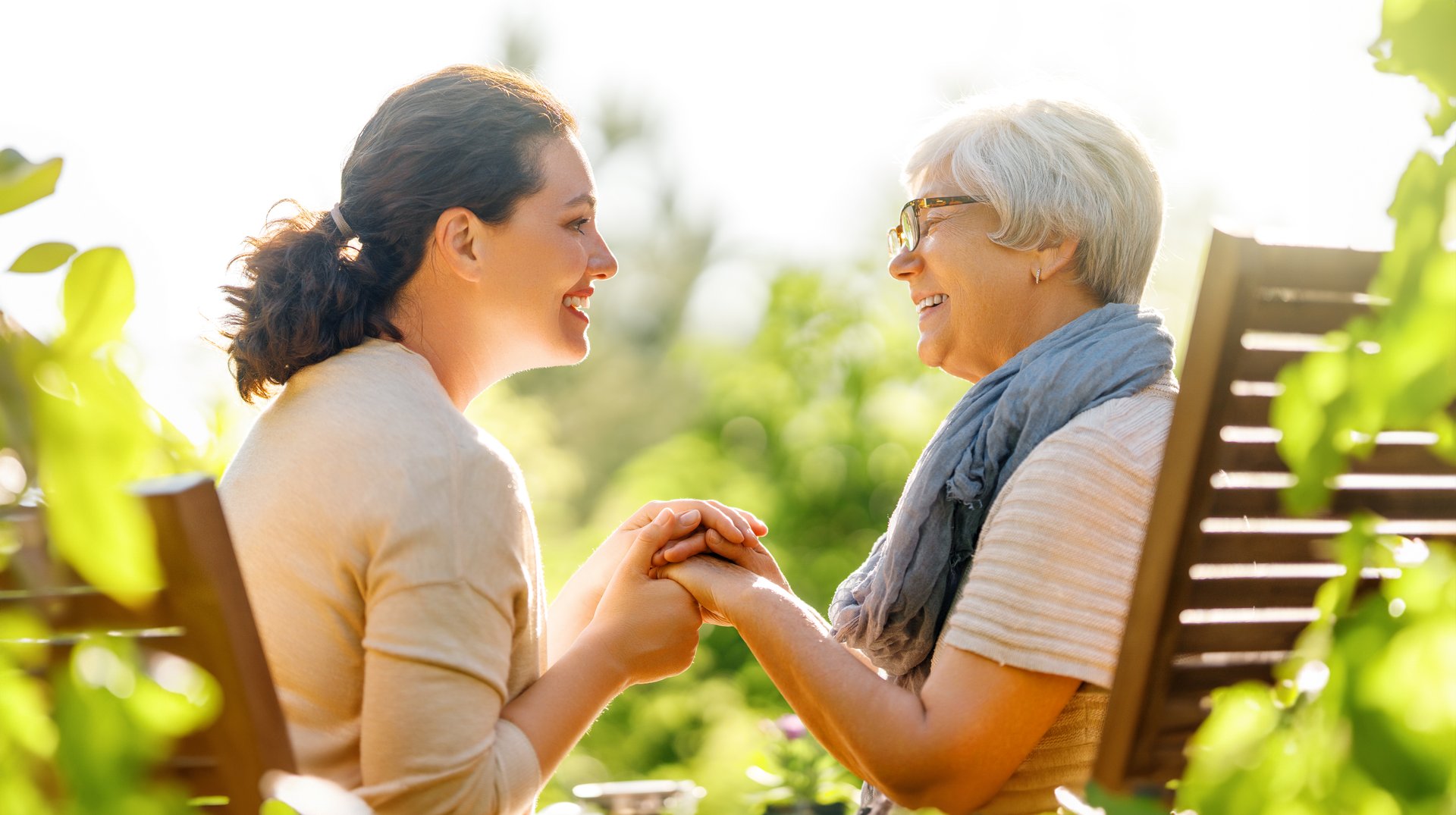 Happy young woman and her mother relaxing in summer morning. Family sitting in the garden and enjoying the conversation.