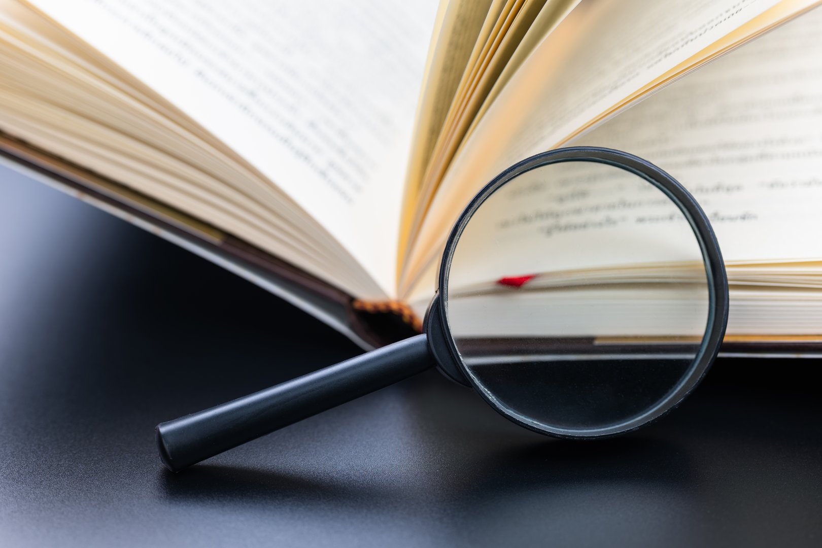 A magnifying glass placed at the opened book, searching for information in the book