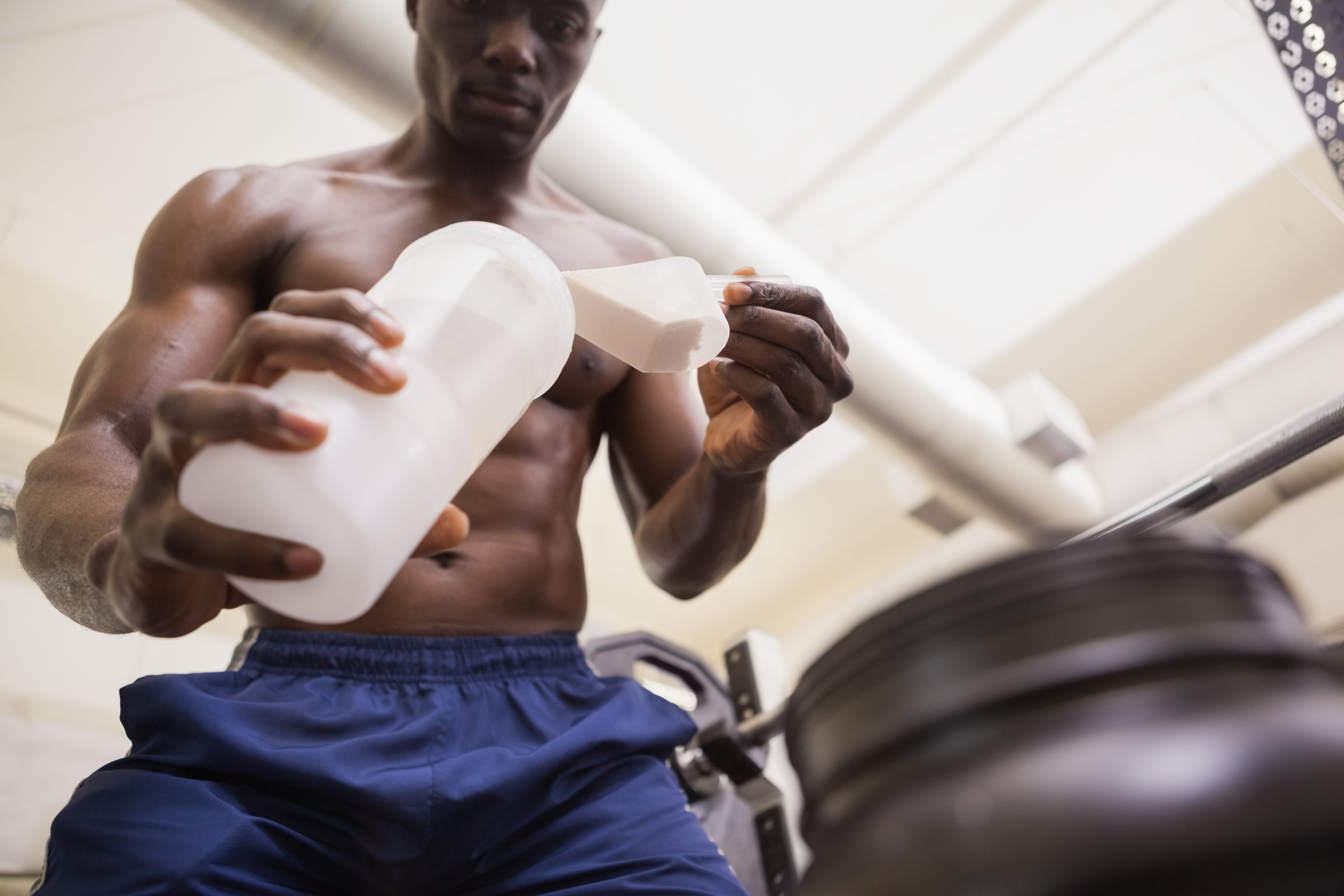 Shirtless body builder scooping up protein powder in gym