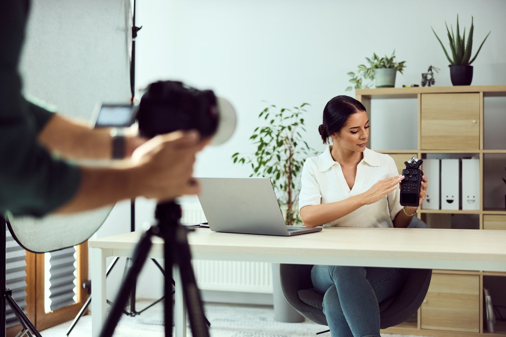 Professional woman filming product review at a desk with camera and laptop.