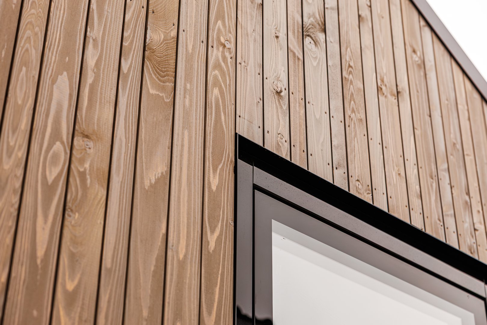 Close-up of a wooden exterior wall with vertical timber cladding and minimalist window, showcasing modern architectural design and sustainable material texture