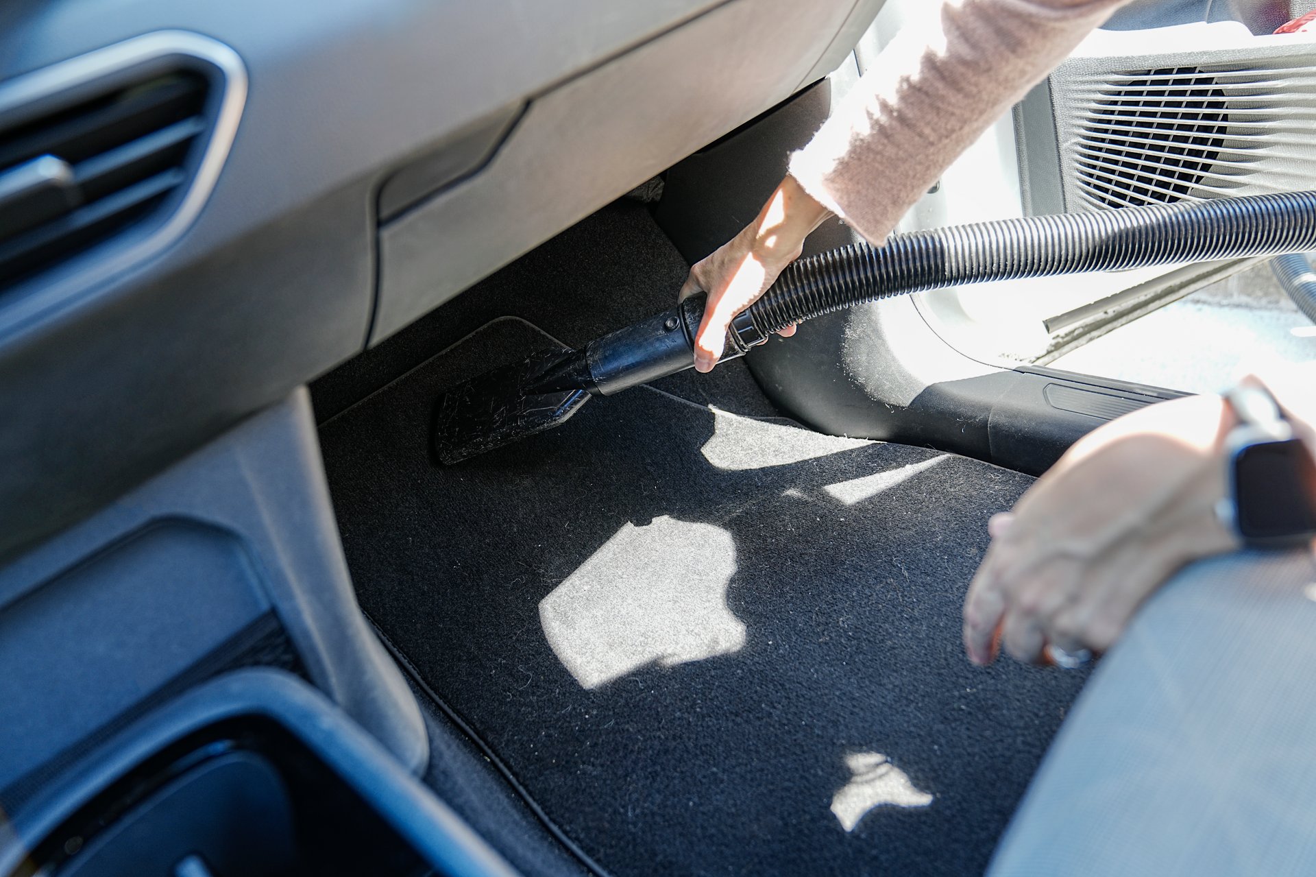 Hand vacuuming the car's floor mats with a precision nozzle.