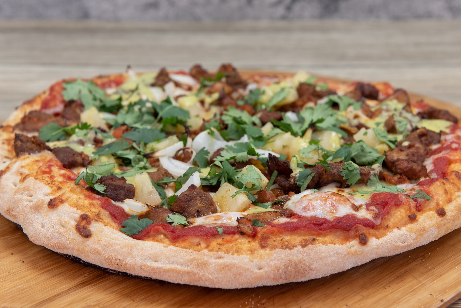 Freshly baked al pastor pizza with delicious meat toppings served on a wooden platter