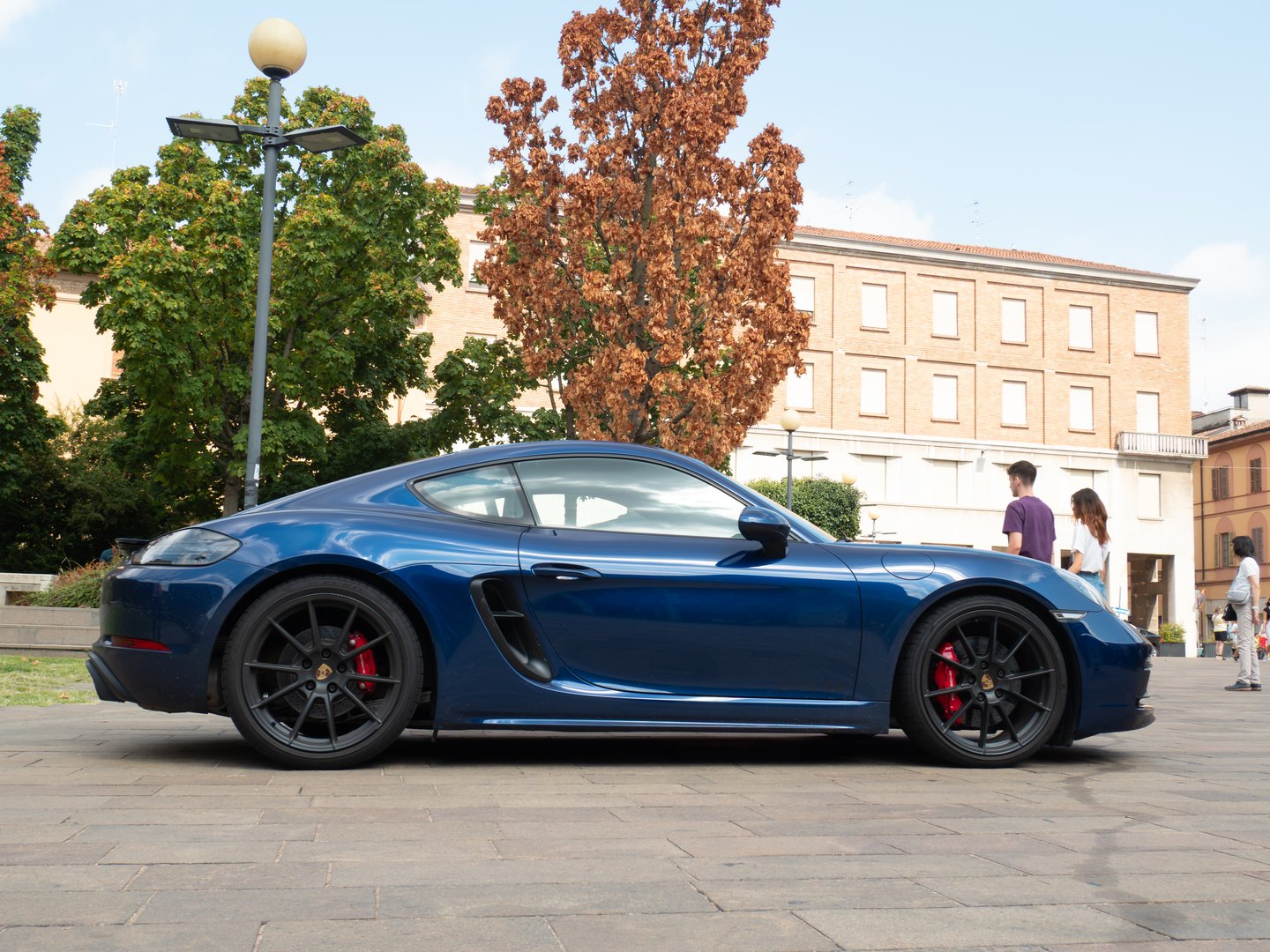 Cremona, Italy August 22nd 2025 Blue Porsche 718 Cayman parked on paved surface, highlighting curved lines and athletic profile from side perspective