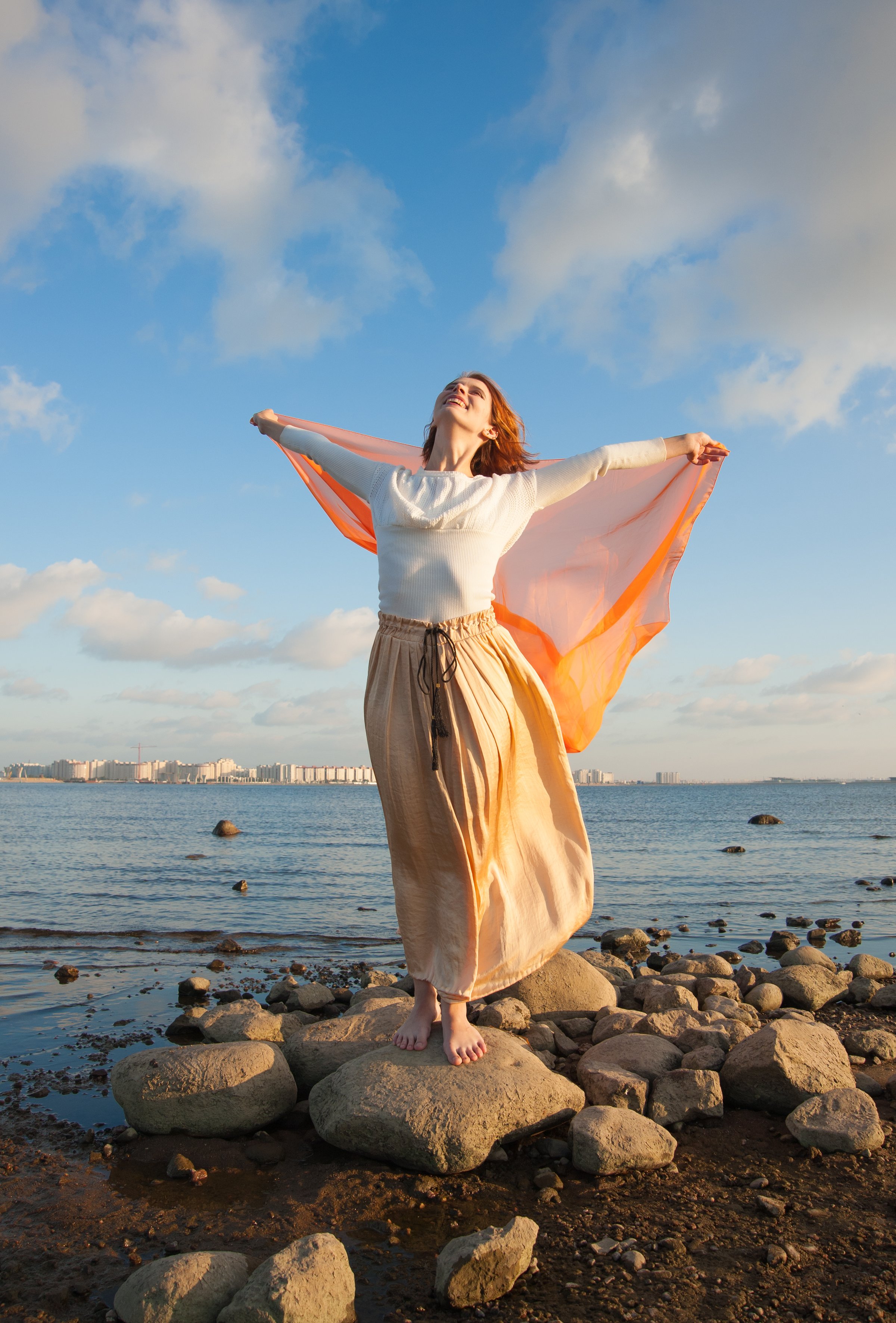 Beautiful young woman holding orange fabric on the wind