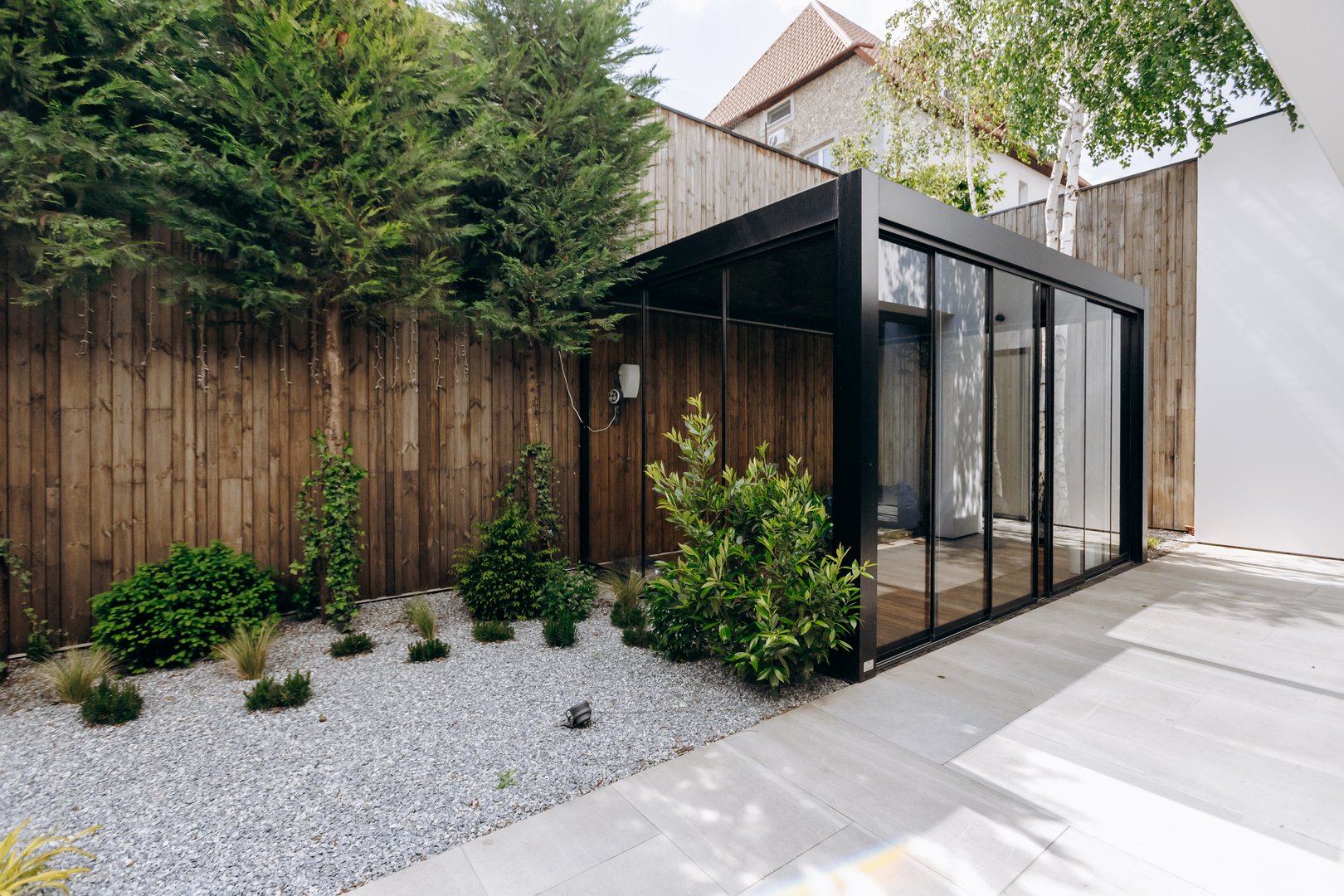 A contemporary designed house featuring an expansive glass wall that offers stunning views, complemented by a wooden fence in the spacious backyard