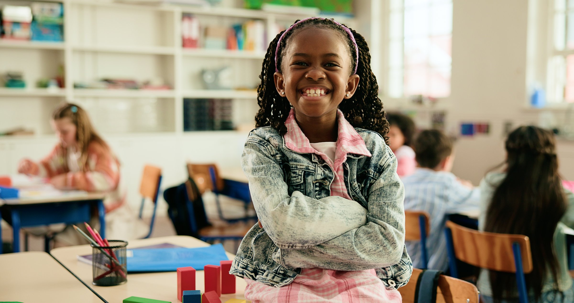 Girl, child and portrait in classroom with arms crossed, smile and confidence for learning at academy. Kid, happy learner and pupil for education, ready or development with pride at elementary school