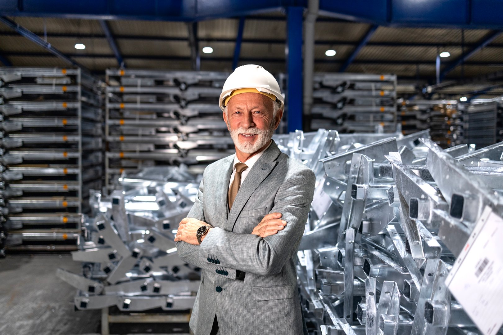 Portrait of senior director with hardhat standing in metal factory production hall.