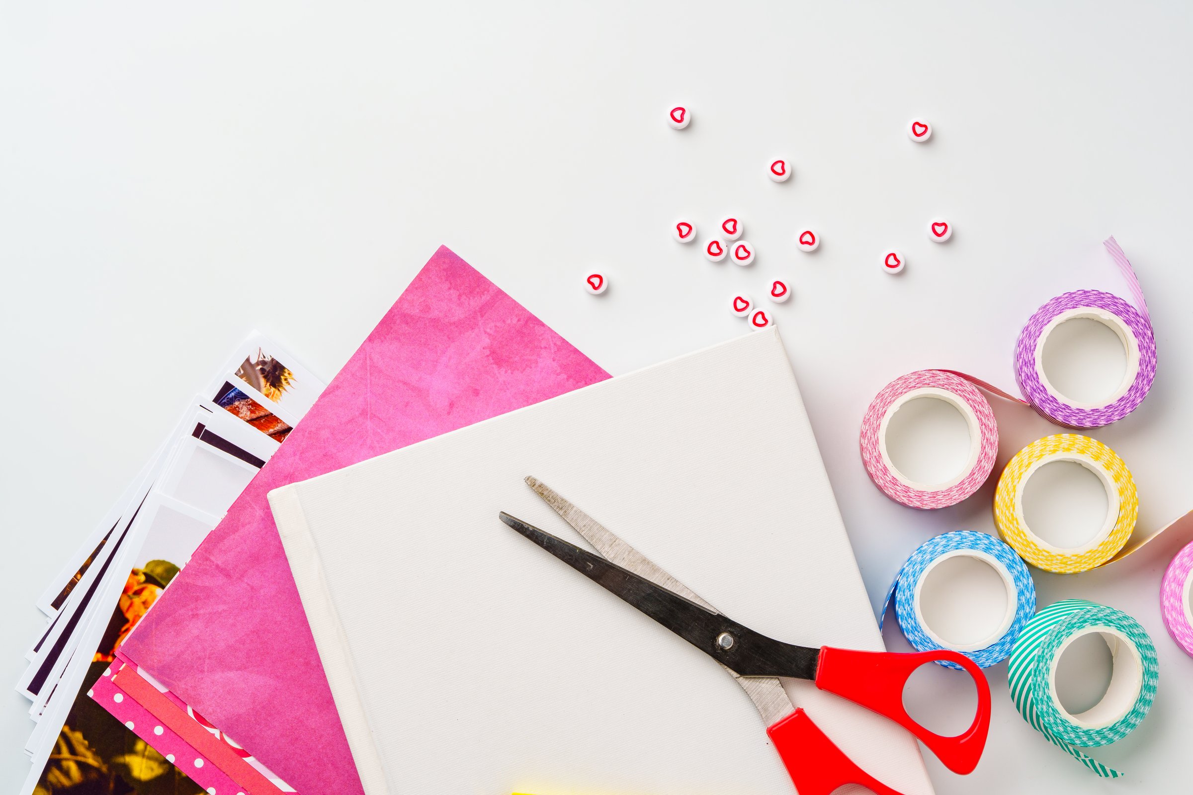 Craft supplies are spread out on a clean workspace. Colorful tape, scissors, and various sheets of decorative paper invite creativity for art or scrapbook projects.