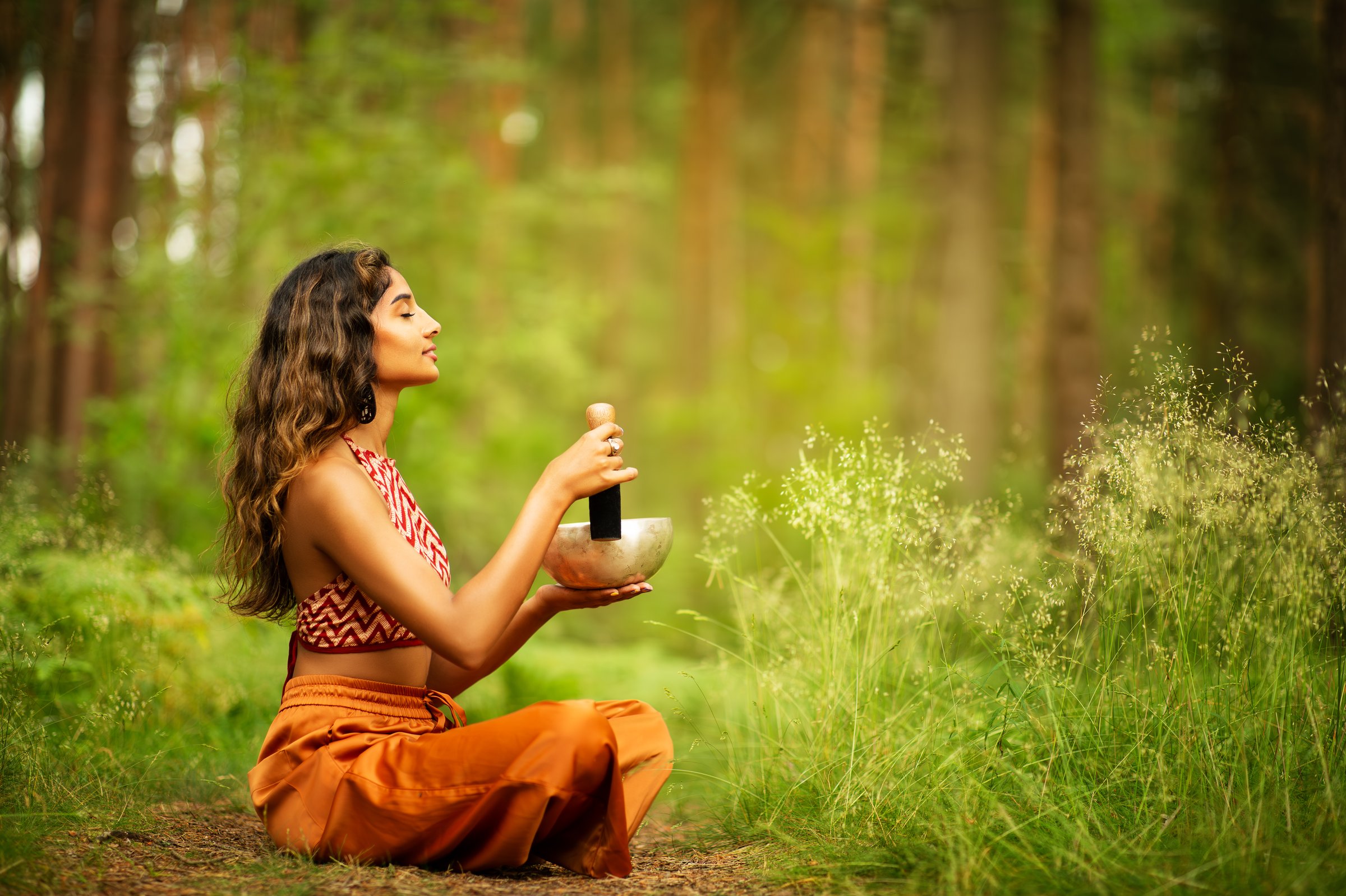 Indian Woman playing Tibetan Singing Bowls with Mallet Outdoors. Relaxing Meditative Music Therapy and Sound Healing. Spiritual Yoga Meditation Practice in Forest