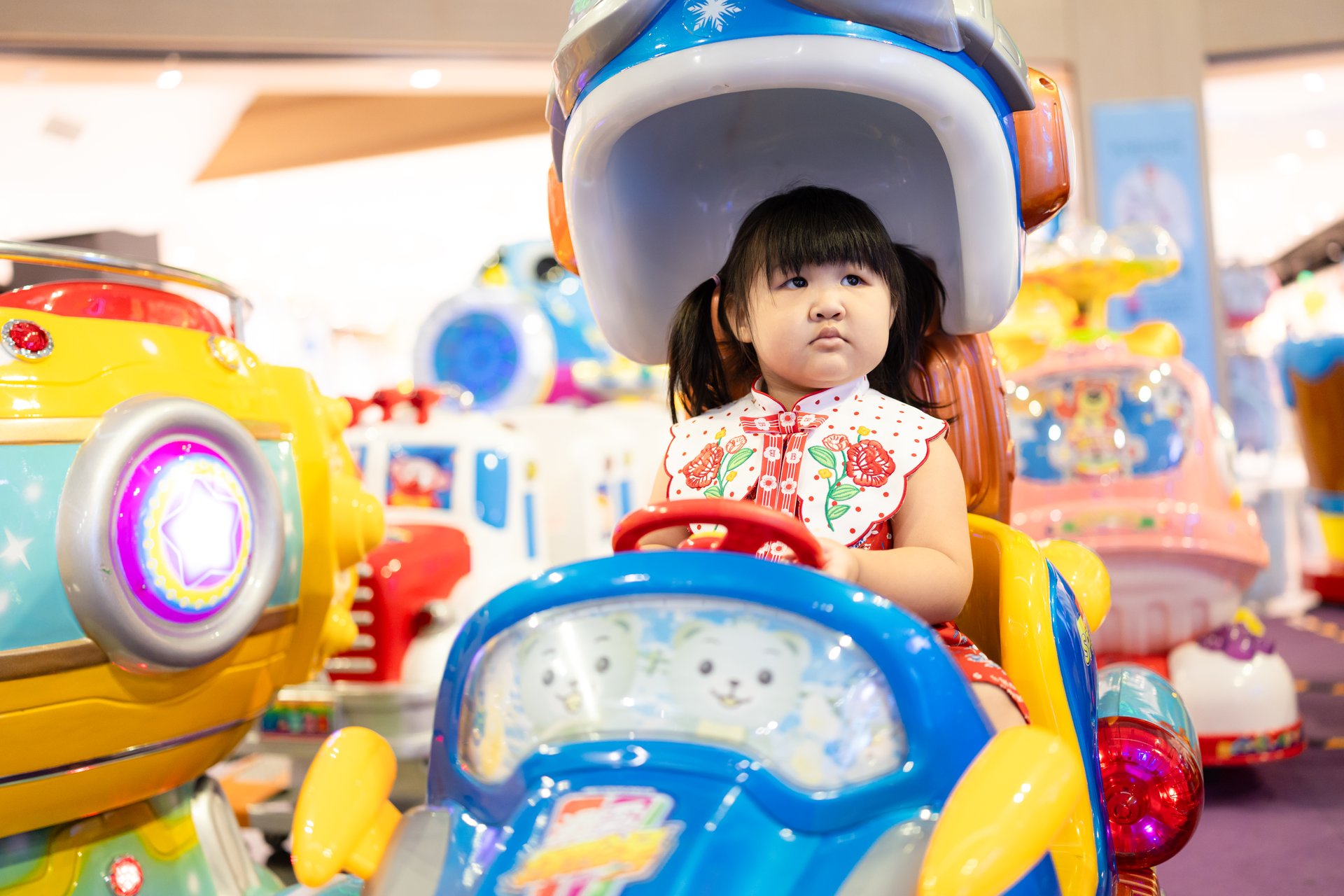 A little girl is sitting on a toy car in a shopping mall,Children driving toy cars,Asian cute children play in mall.