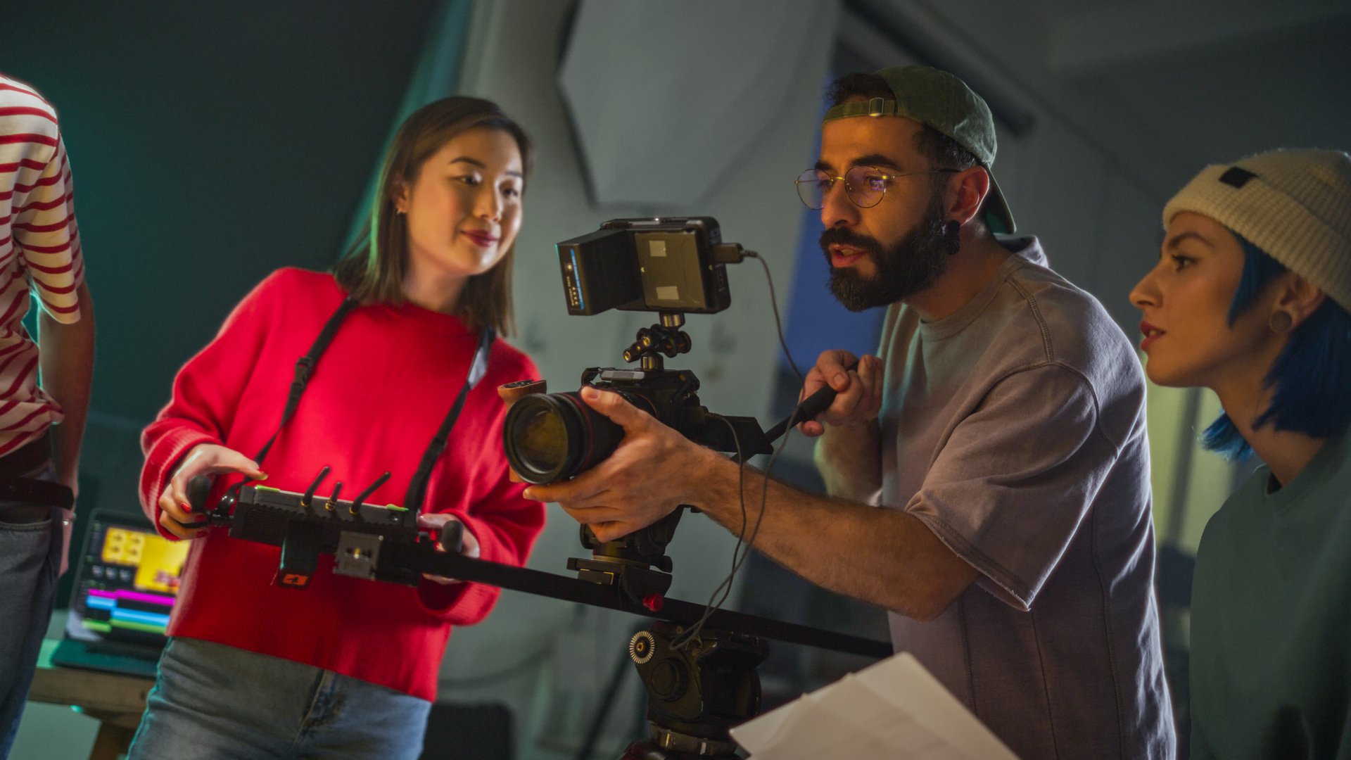 Young Asian Female And Middle Eastern Male Cinematographer Collaborate On Film Set, Adjusting Camera Equipment, Surrounded By Crew, Focused On Capturing Engaging Content For Media Production.