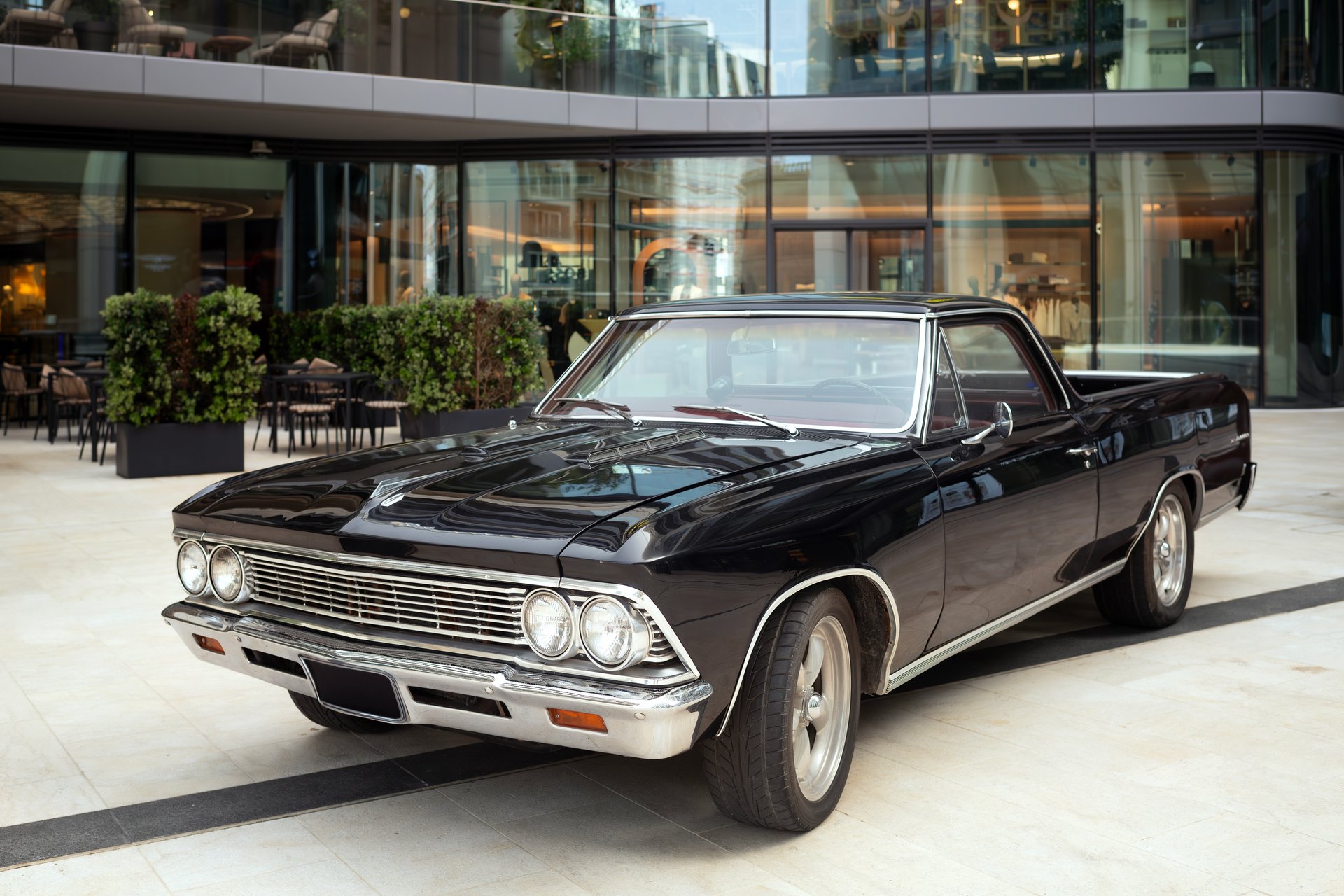 Vintage black car parked in a modern courtyard. Sharp focus on headlights and front design creates a depth of field effect with detailed foreground and softly blurred background.