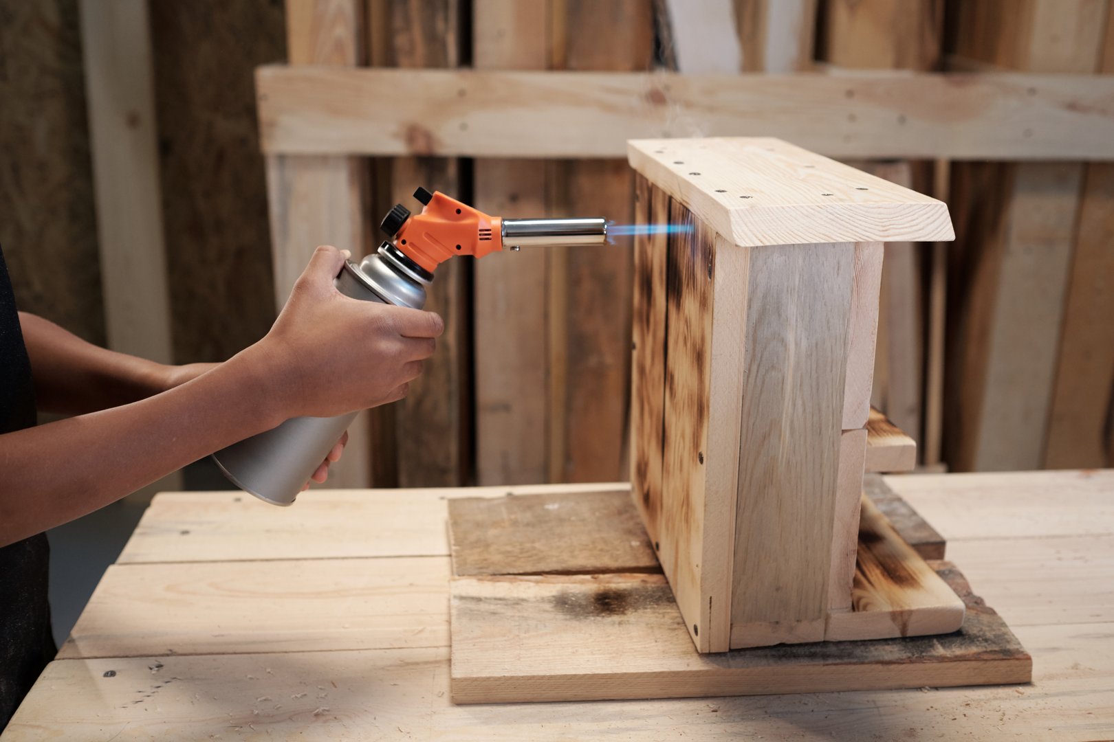 Side view closeup of African-American boy decorating wooden birdhouse in workshop with gas torch