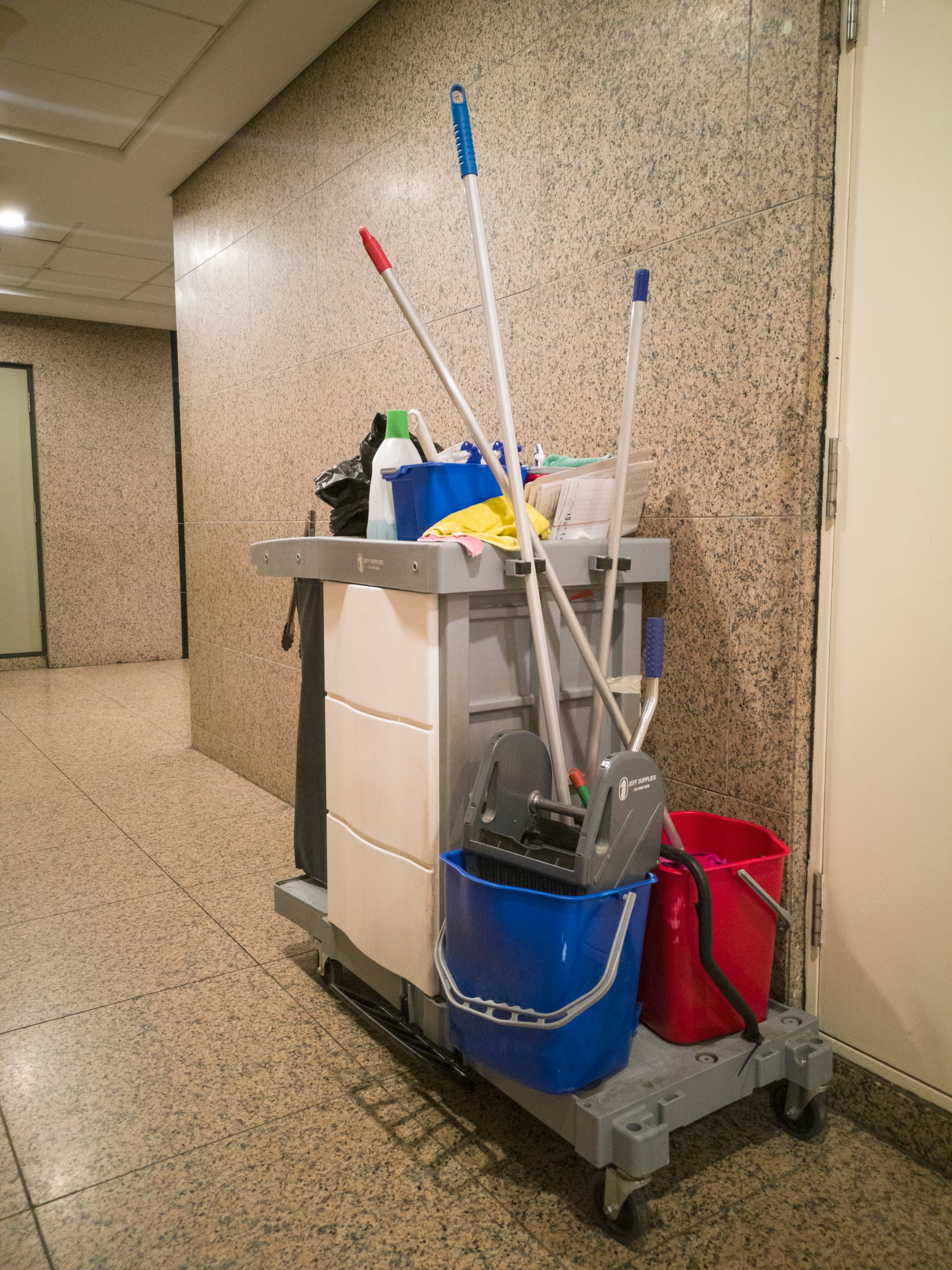 Close-up view of a cleaning utility janitorial or cleaner cart along a quiet office corridor, it has storage for all cleaning tools and detergent.