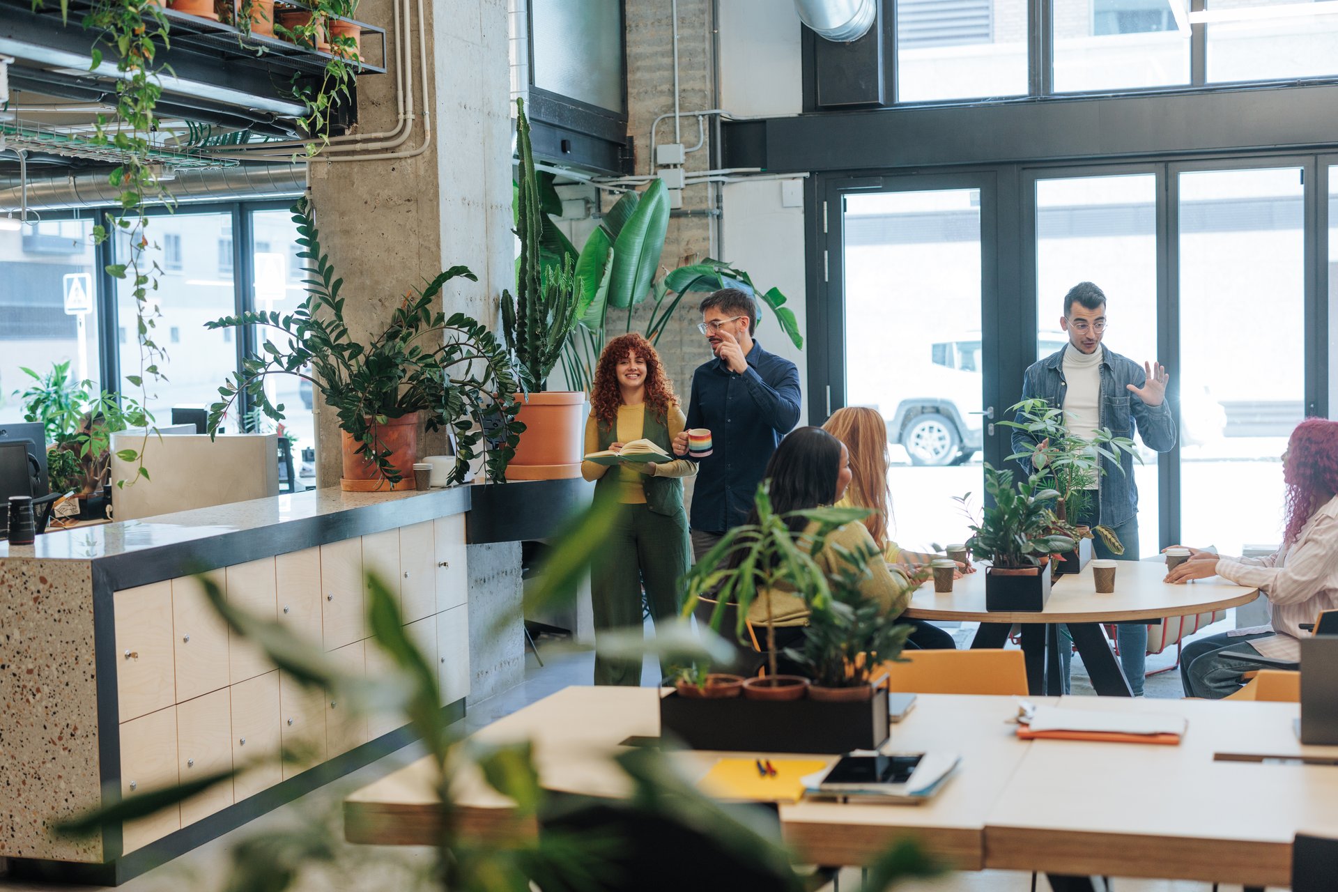 Businesspeople collaborating and sharing ideas in a vibrant, plant-filled co-working space, fostering a positive and productive work environment