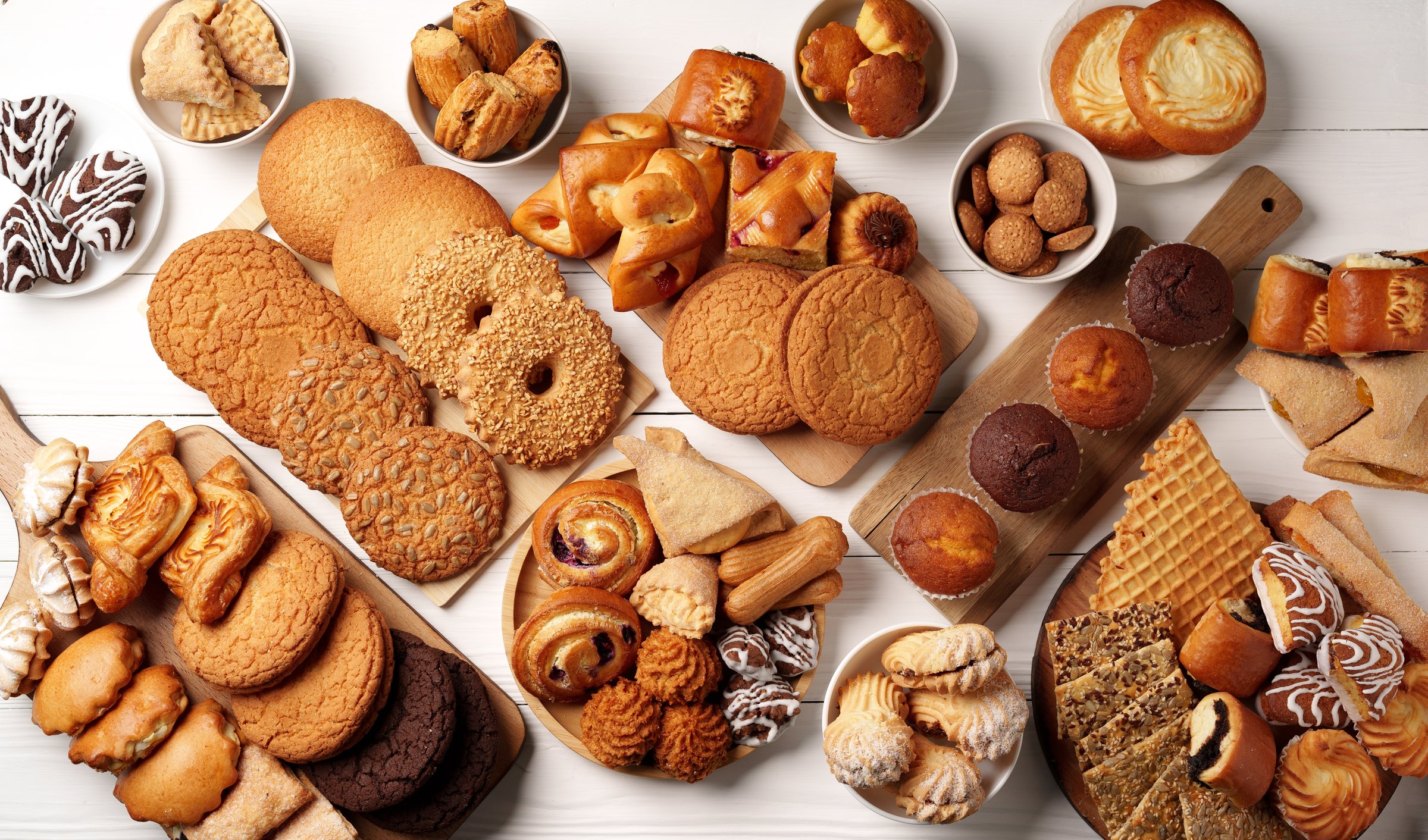 A beautiful spread of freshly baked goods is arranged on a wooden surface, showcasing cookies, pastries, and sweet treats in diverse shapes and flavors.