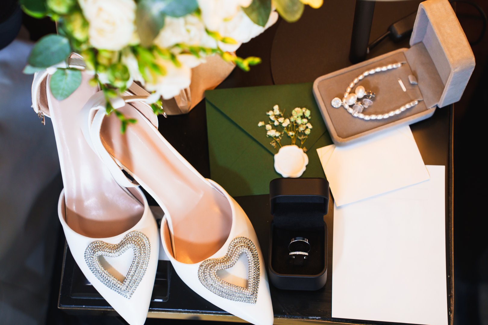 Bridal accessories are arranged on a table, featuring stylish shoes with heart designs, jewelry, a ring box, and a bouquet. An elegant atmosphere sets the tone for the special day.