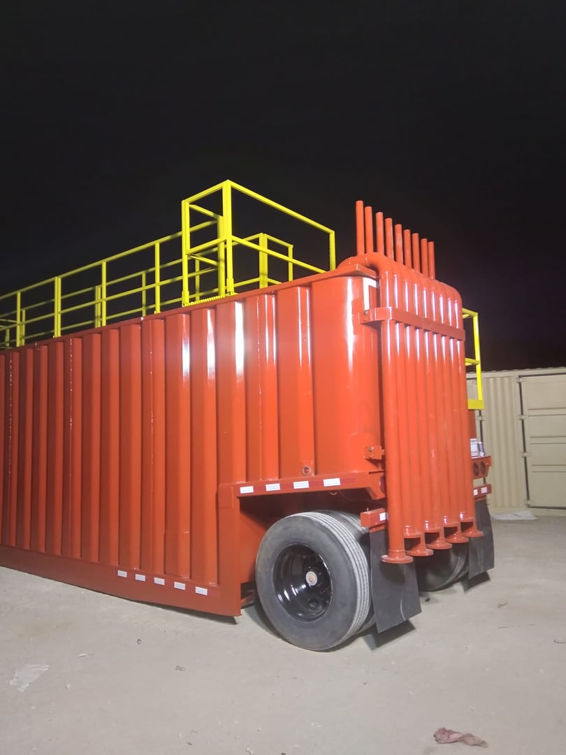 Large red container trailer with yellow railing parked on a dirt surface at night.