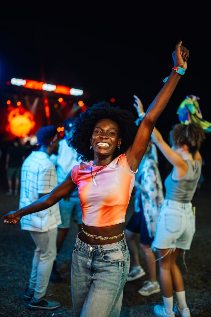 Vibrant scene captures a woman dancing energetically at a nighttime music festival. The colorful lights and lively crowd create an atmosphere of excitement and celebration