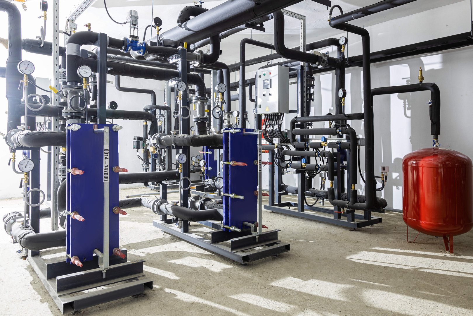 Industrial basement with heating pipes, pressure gauges, valves and heat exchangers.
